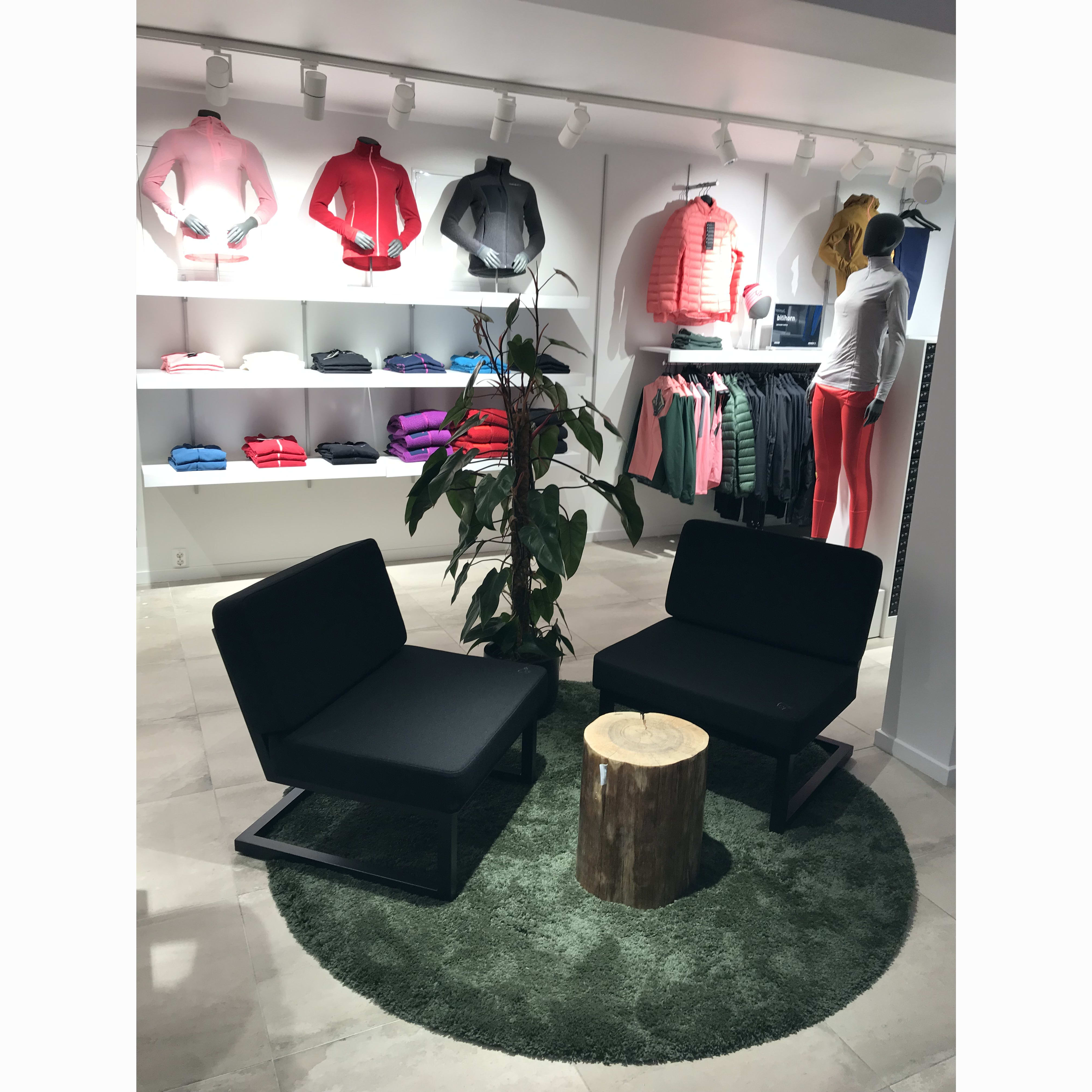Norrøna clothing display next to two black chairs and a log table on a green rug.