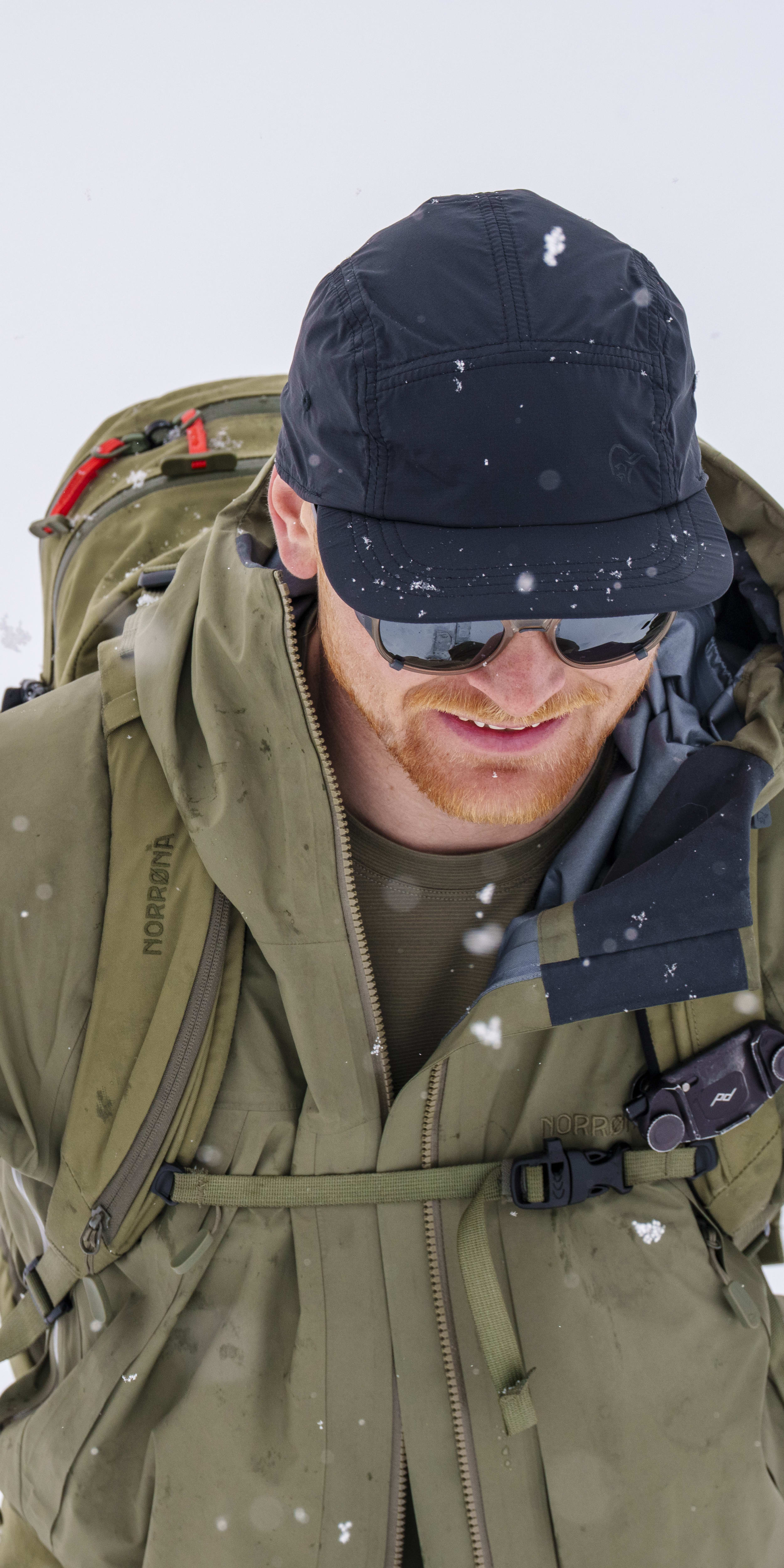 A person in a Norrøna jacket and cap with a backpack looking down in the snow.