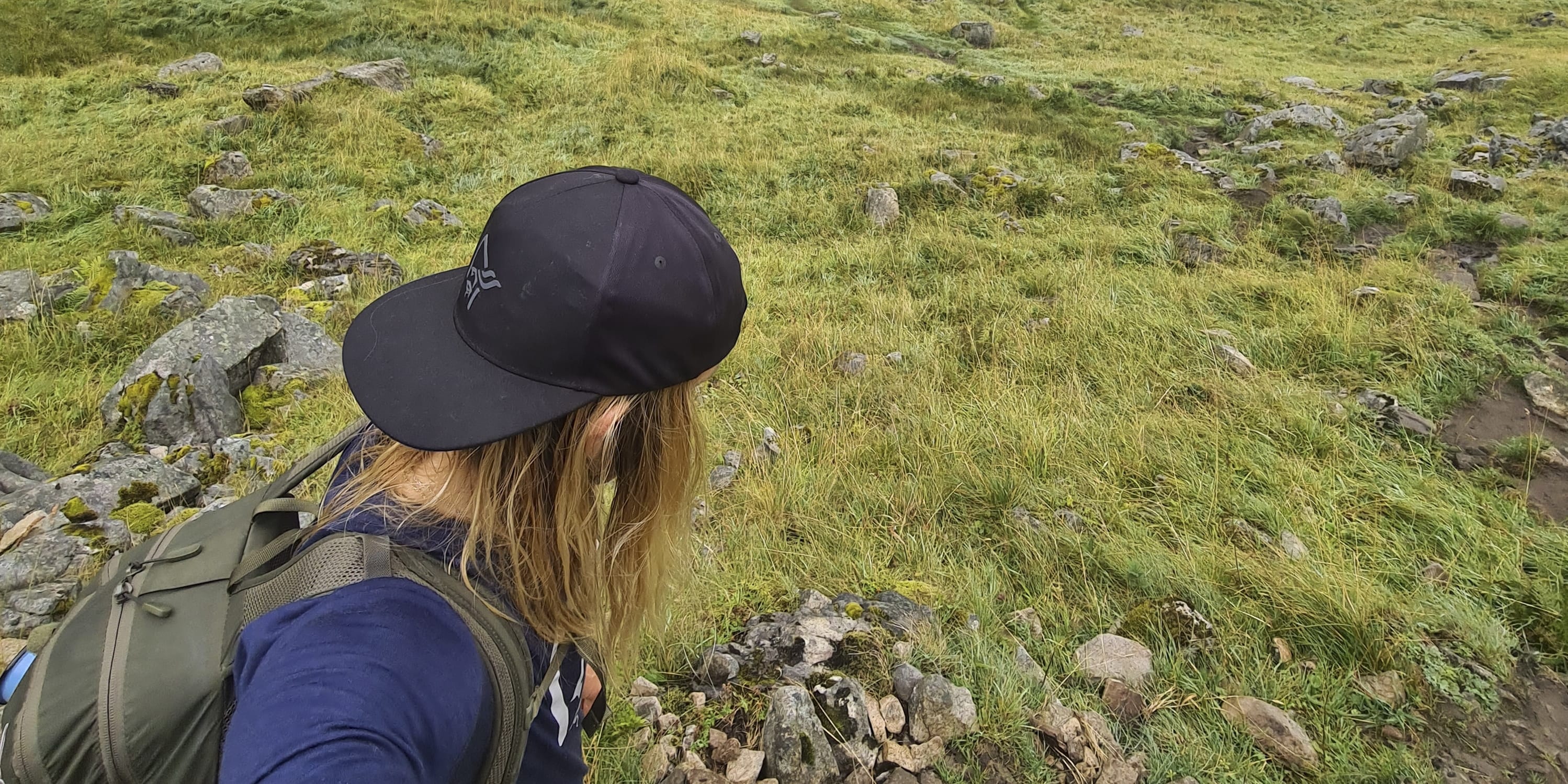 Person wearing a Norrøna outfit and a backpack, looking at a beach with a mountain in the background.