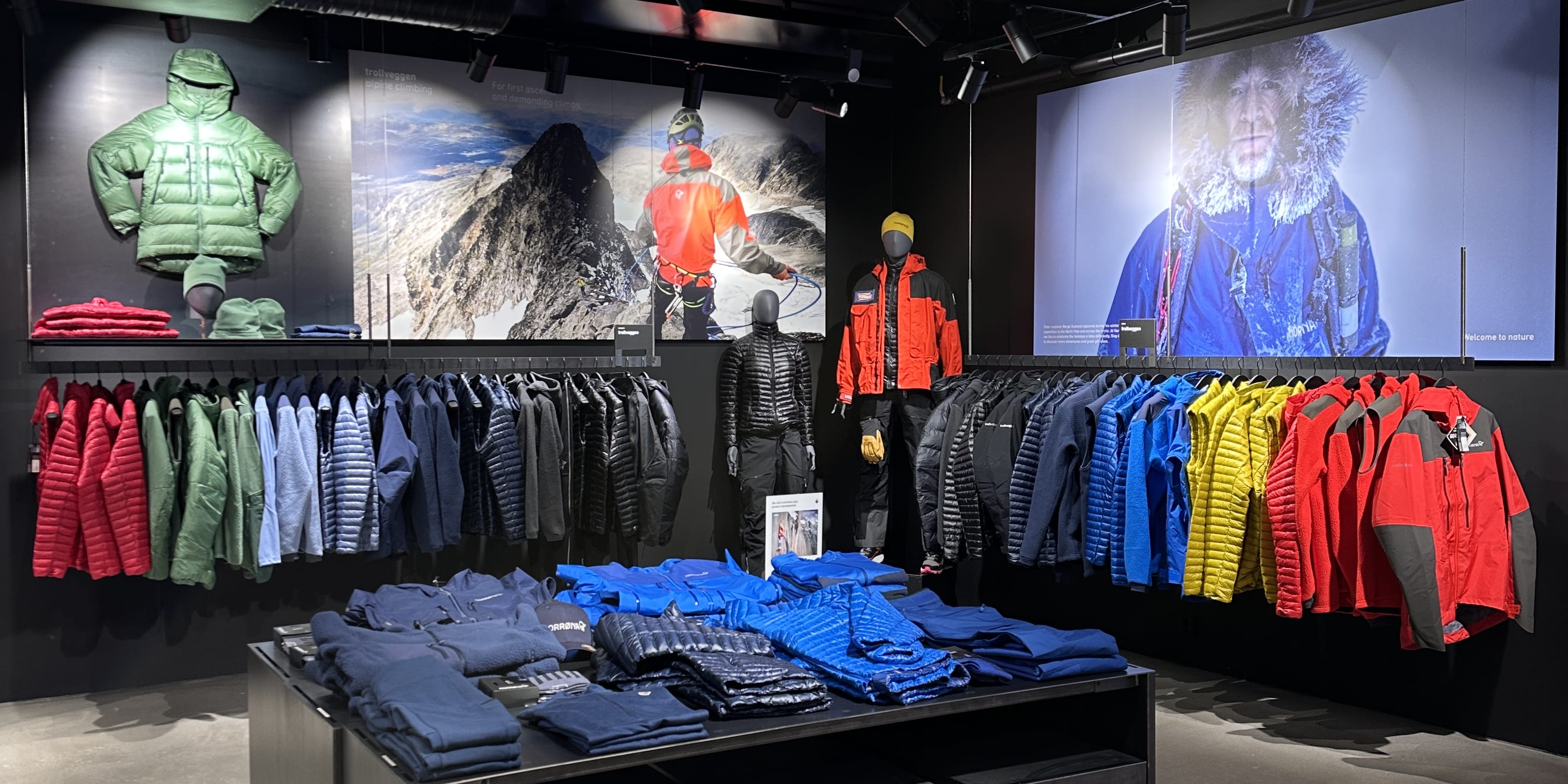 An angled view of a Norrøna retail display showcasing colorful outdoor apparel. Mannequins and landscape posters accent the stacked clothing.
