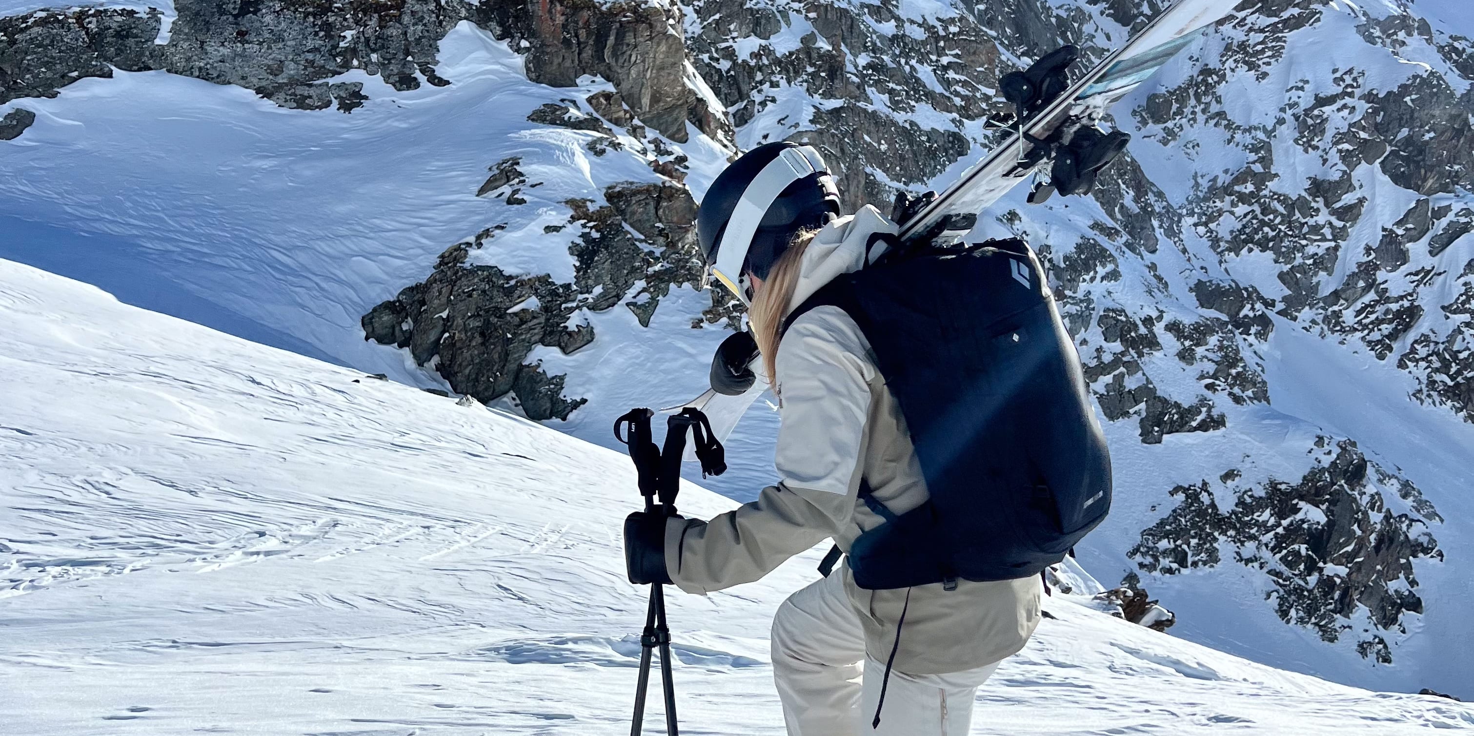 A person wearing a Norrøna ski suit and a helmet is hiking uphill in a snowy mountain landscape. 
