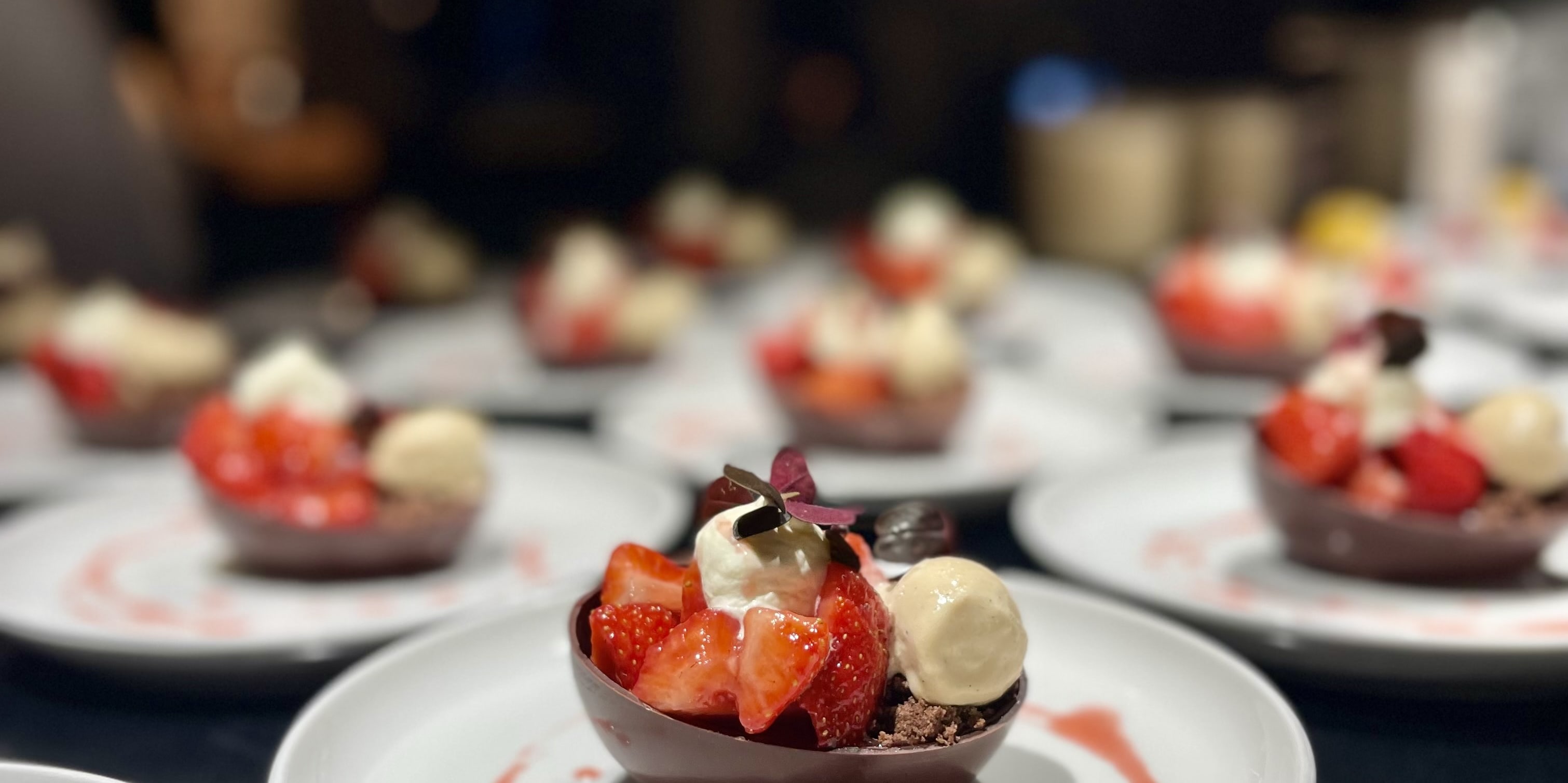 A close-up of a chocolate dessert bowl with strawberries, whipped cream and a drizzle of sauce on a white plate.  
