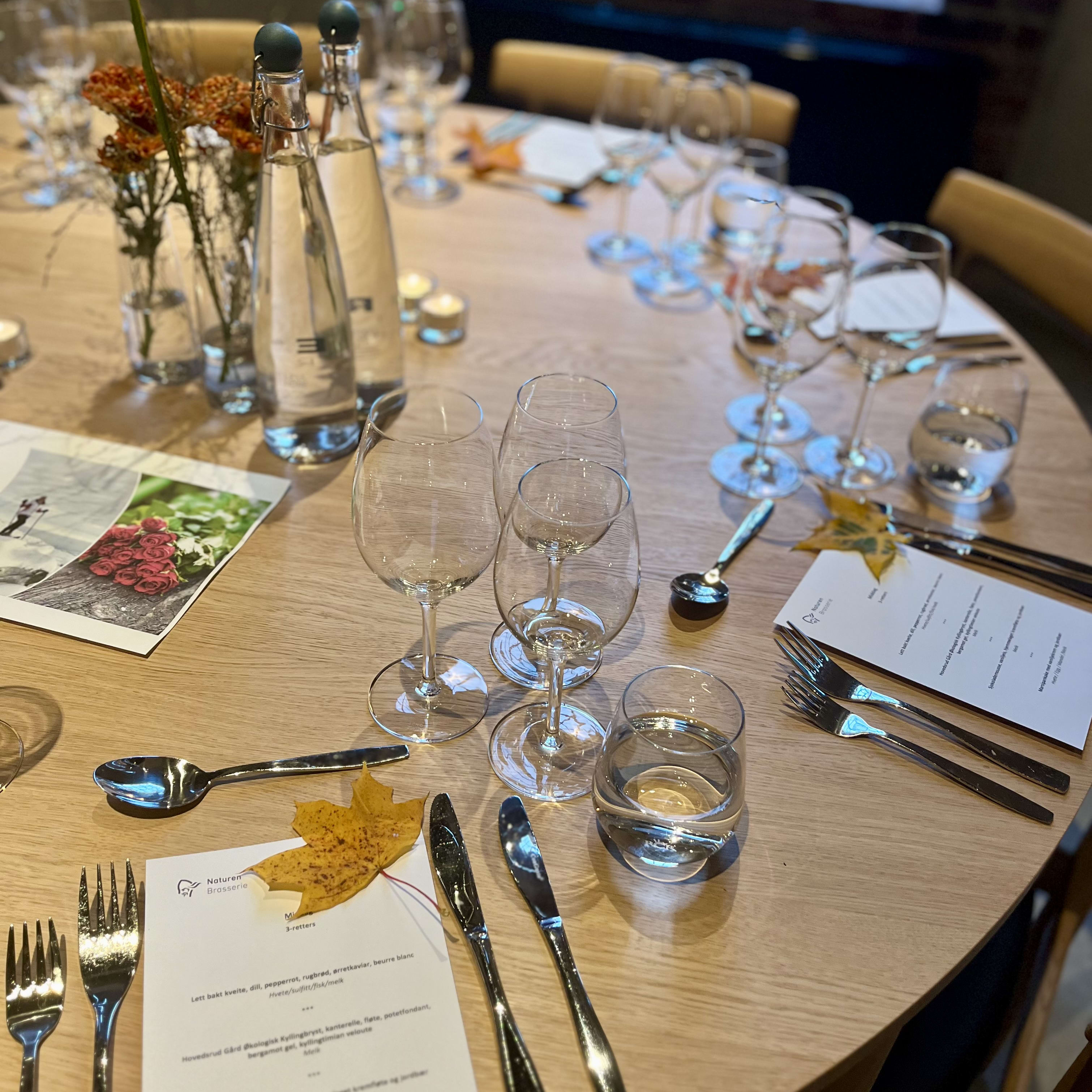 A table set for a meal with wine glasses, silverware, and a menu. There is a fall leaf on the table.