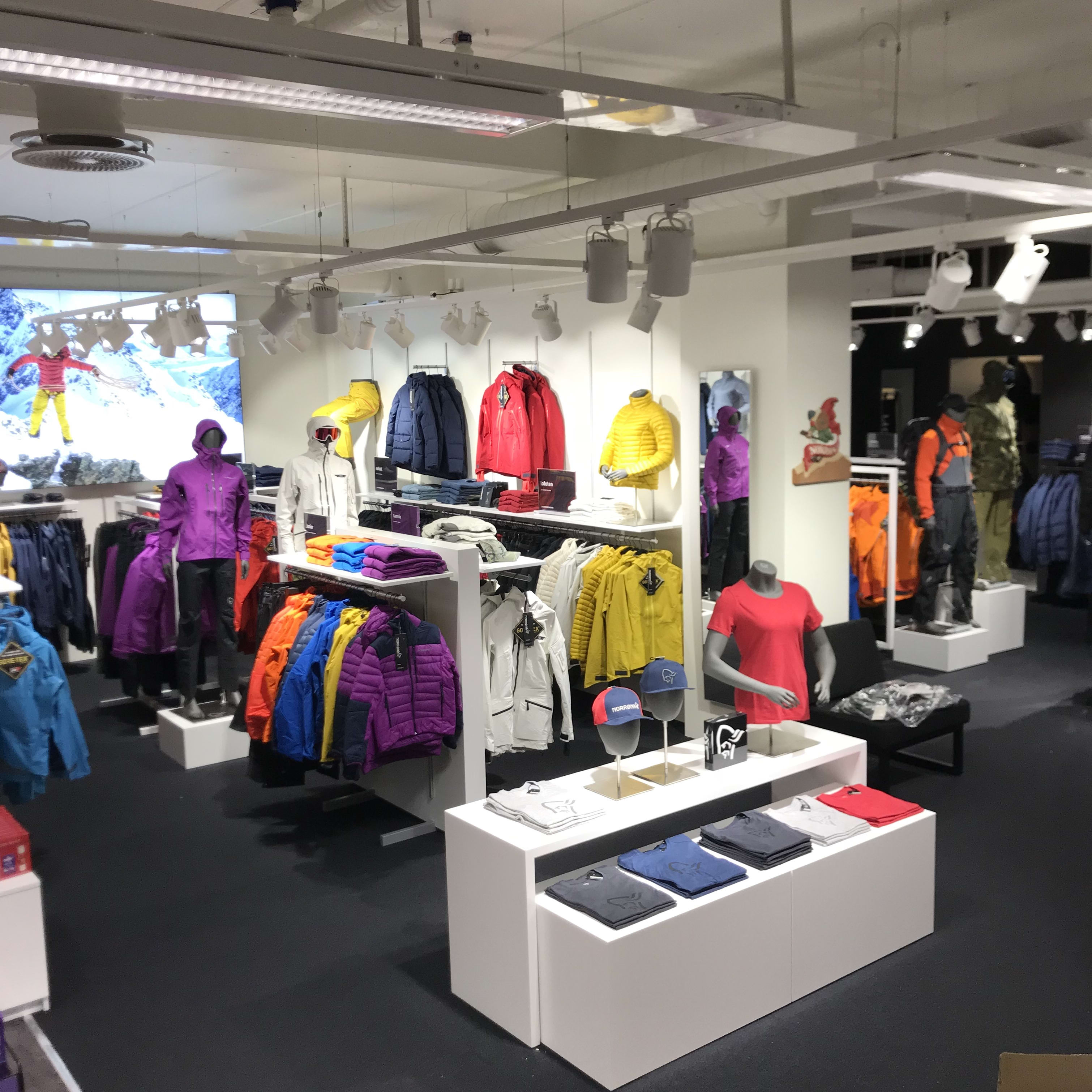 A Norrøna clothing store with racks of jackets, a mannequin, and folded t-shirts on a white table.