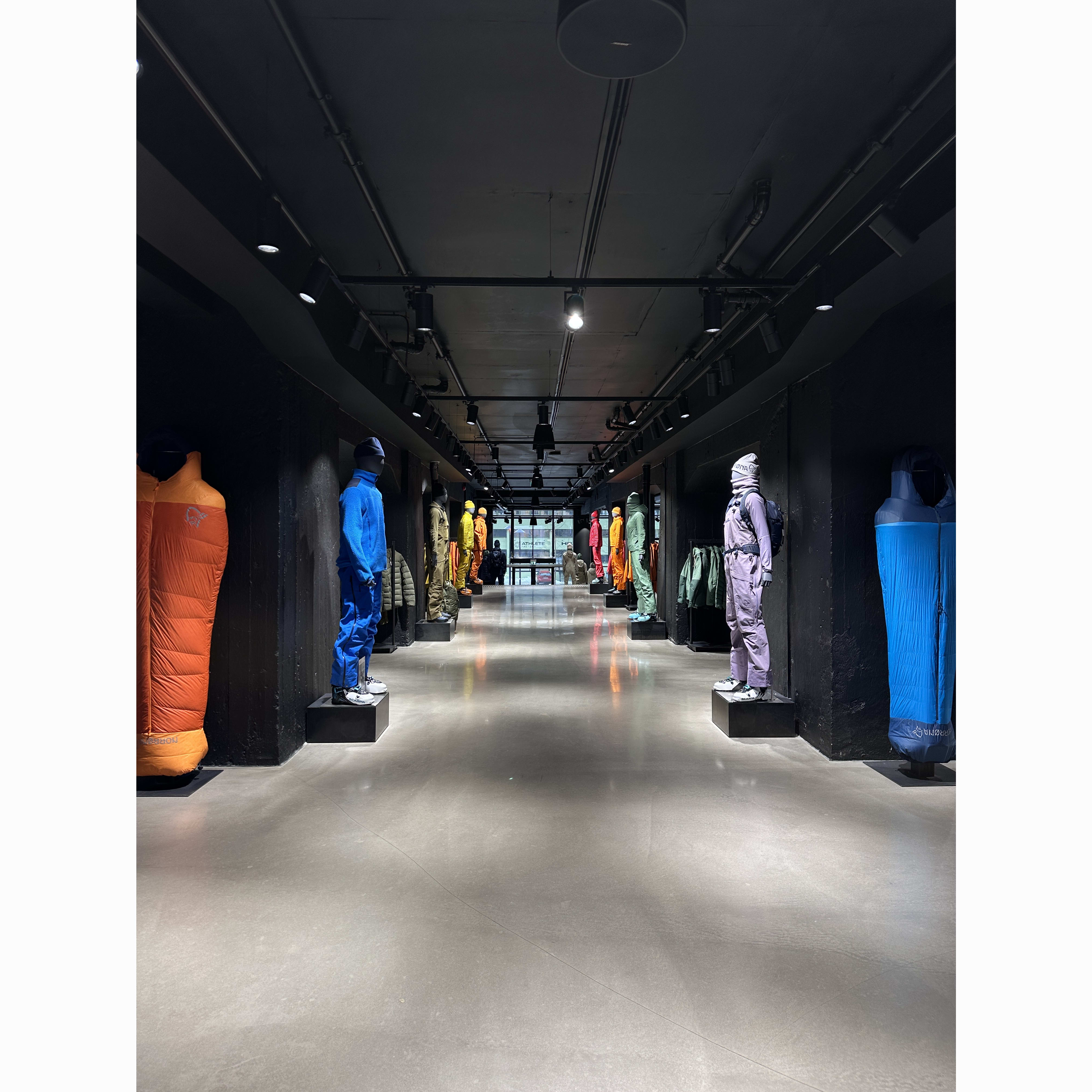 Retail display with rows of colorful Norrøna outdoor clothing and sleeping bags on shelves, viewed from a low angle.