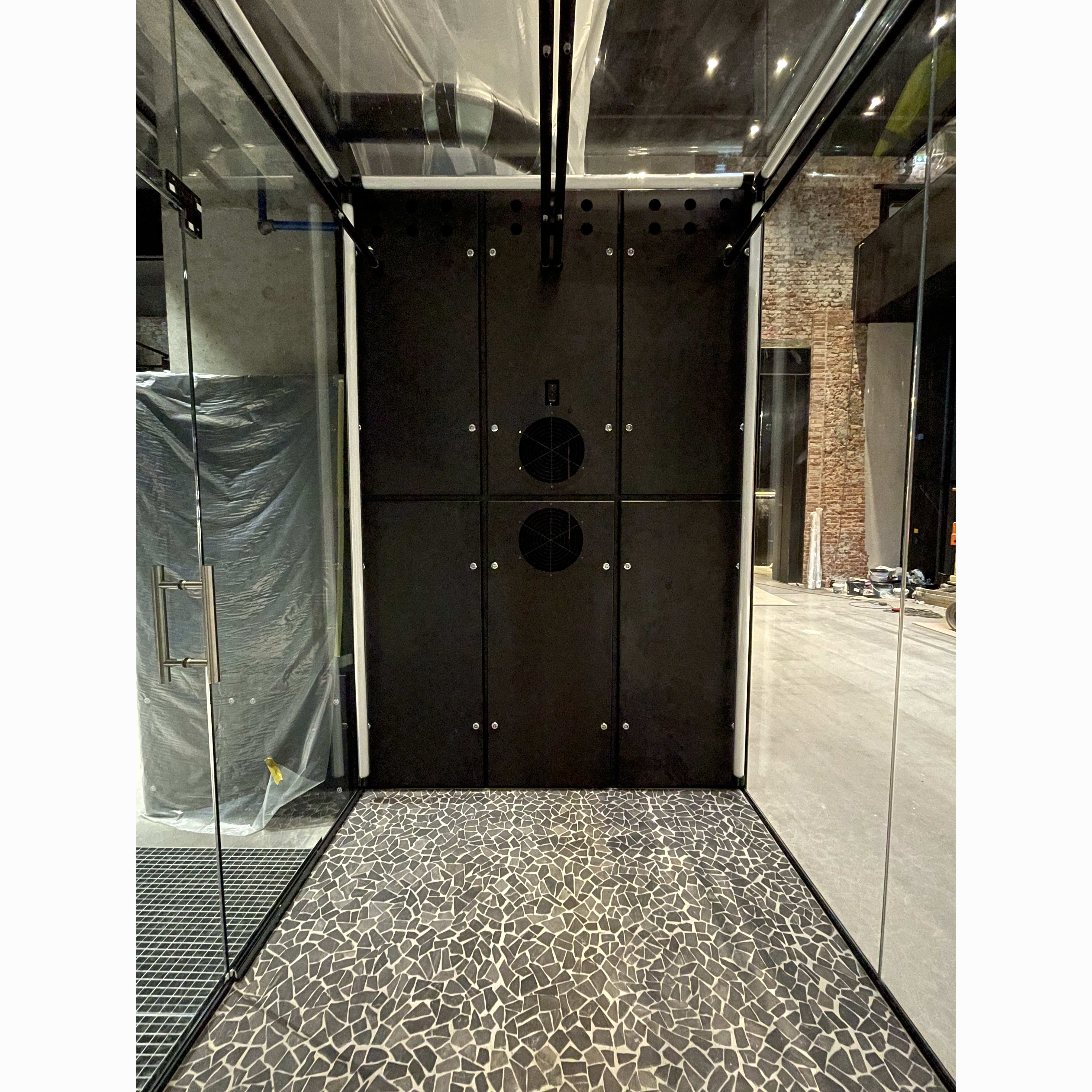 A black panel with two ventilation fans and screws. To the right of the panel is a floor covered in a dark mosaic tile pattern.