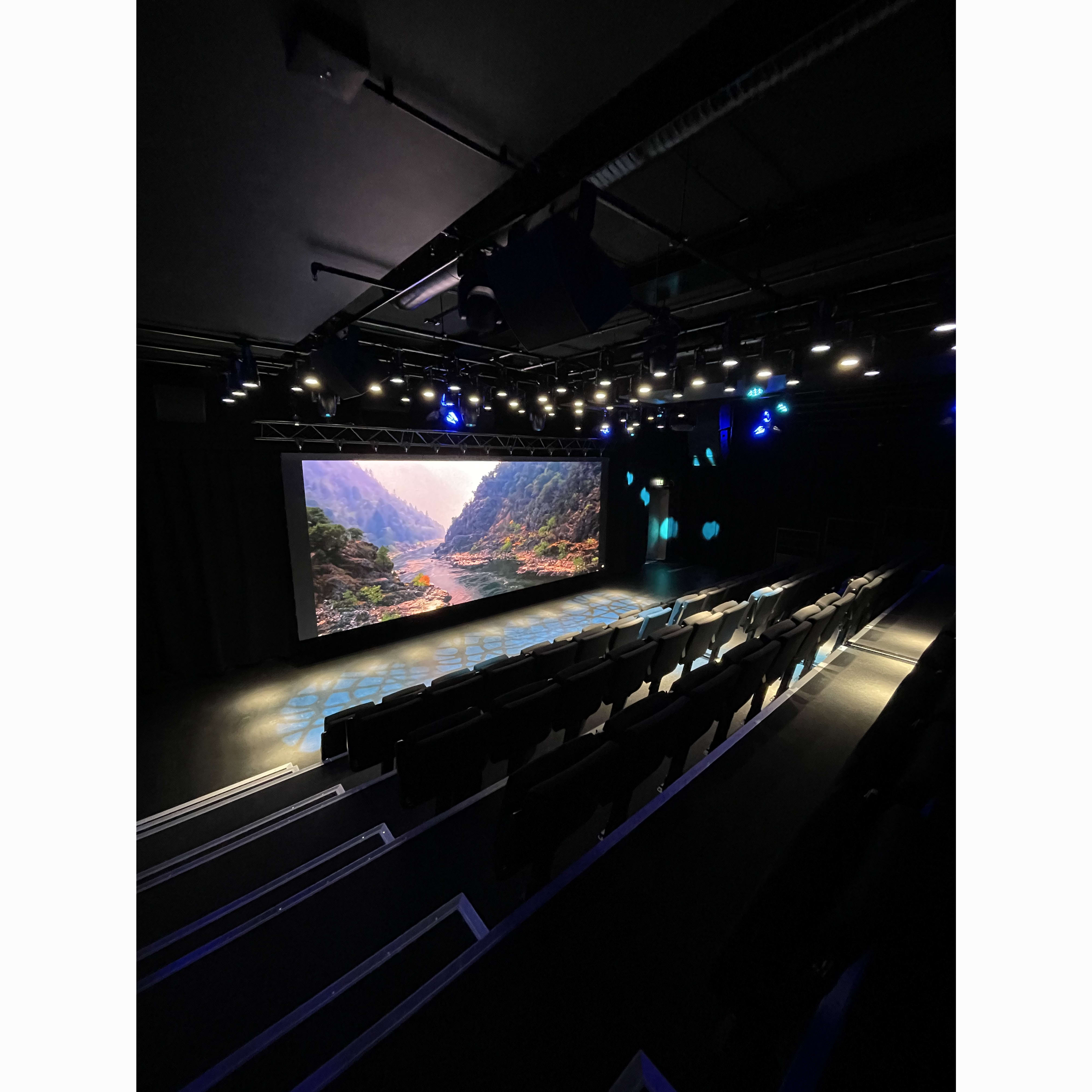 A dark room with a projector screen showing a landscape. Lights shine on a set of bleacher-style seats.