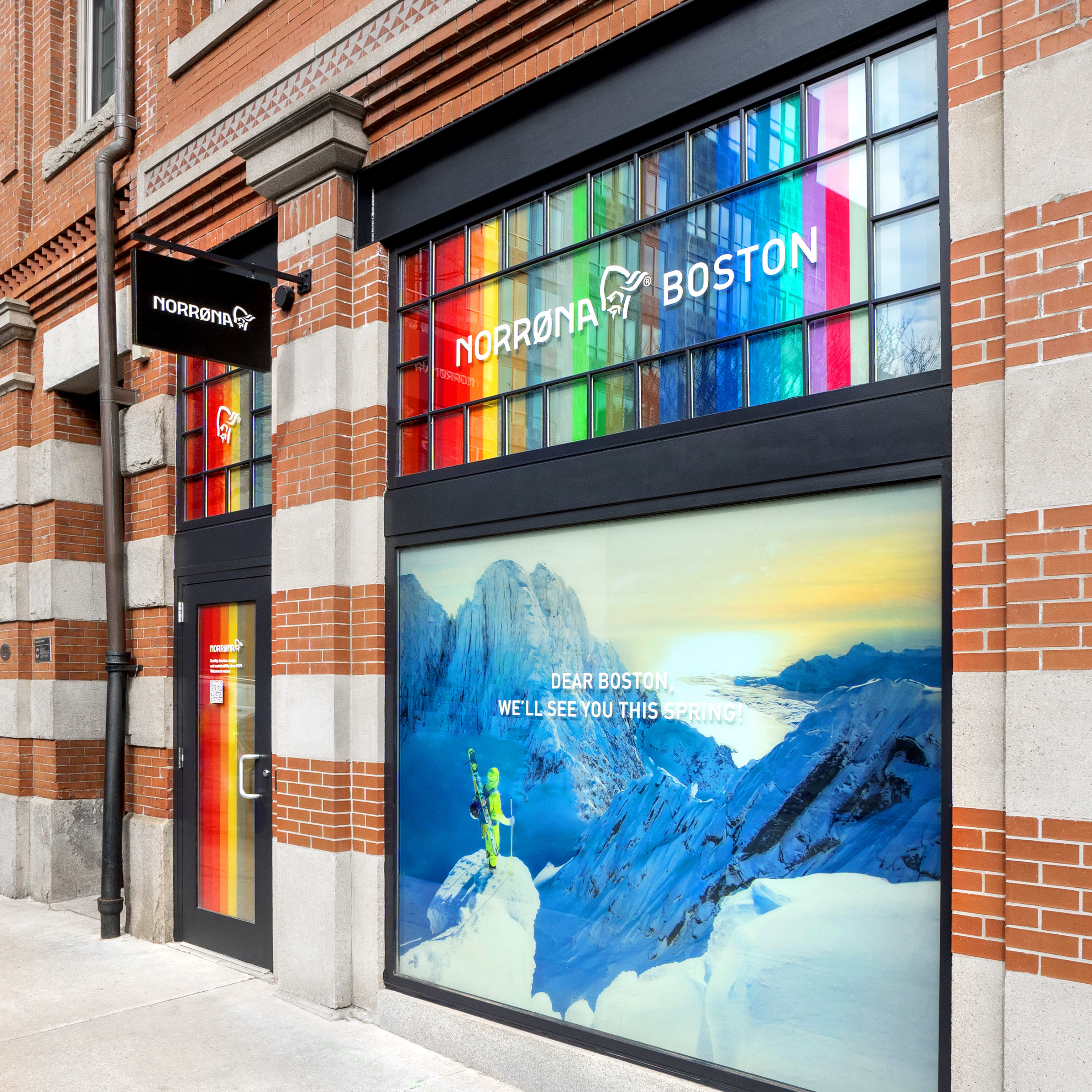 A storefront with the Norrøna logo, "Norrøna Boston" in white text and a rainbow background. The storefront also has a window displaying a mountain scene, a skier, and the text "Dear Boston, We'll See You This Spring!"