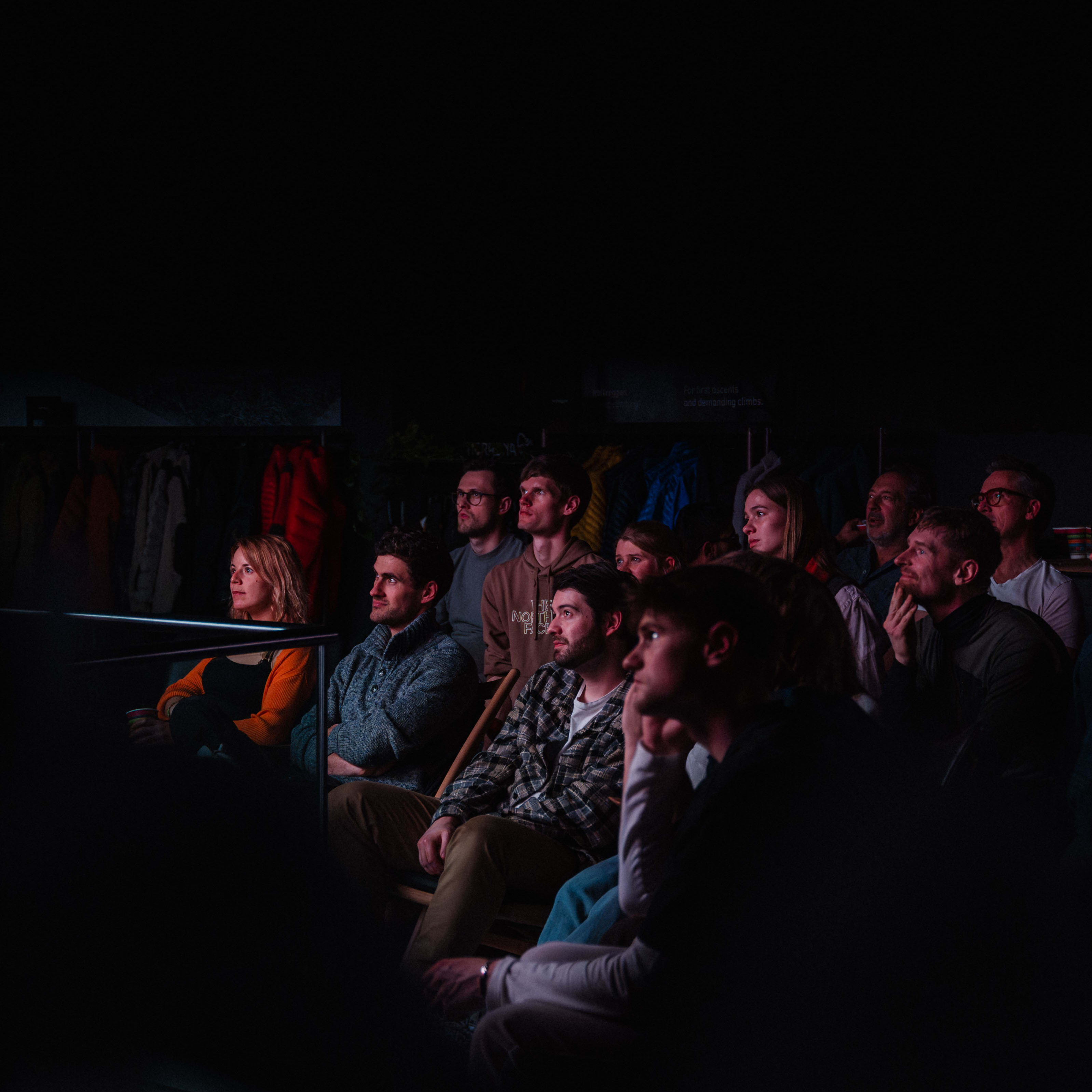 An attentive audience wearing Norrøna clothing watches a presentation in a dimly lit room.
