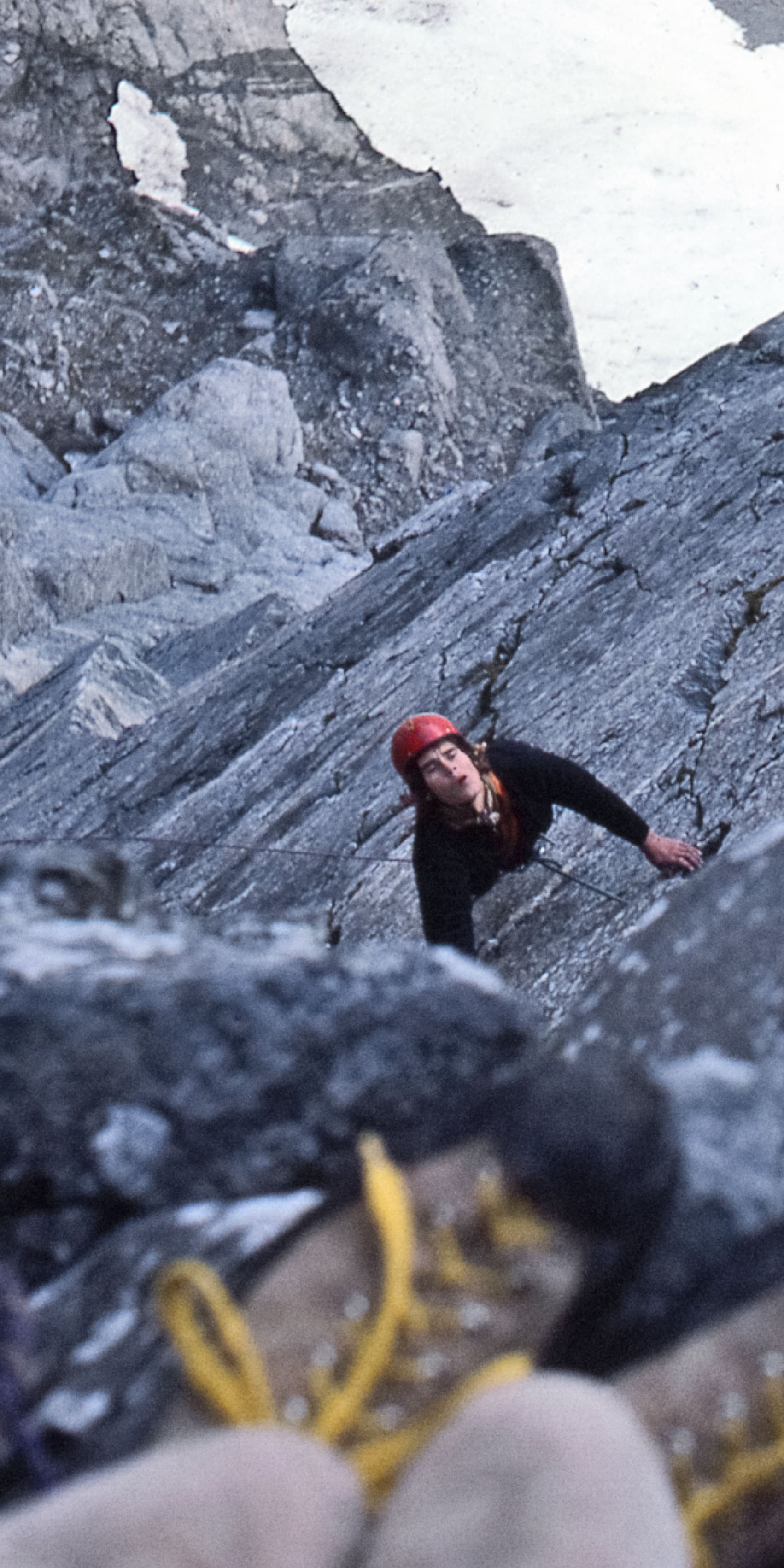 A rock climber with a red helmet is ascending a steep rock face.  The climber is looking up at the next move.