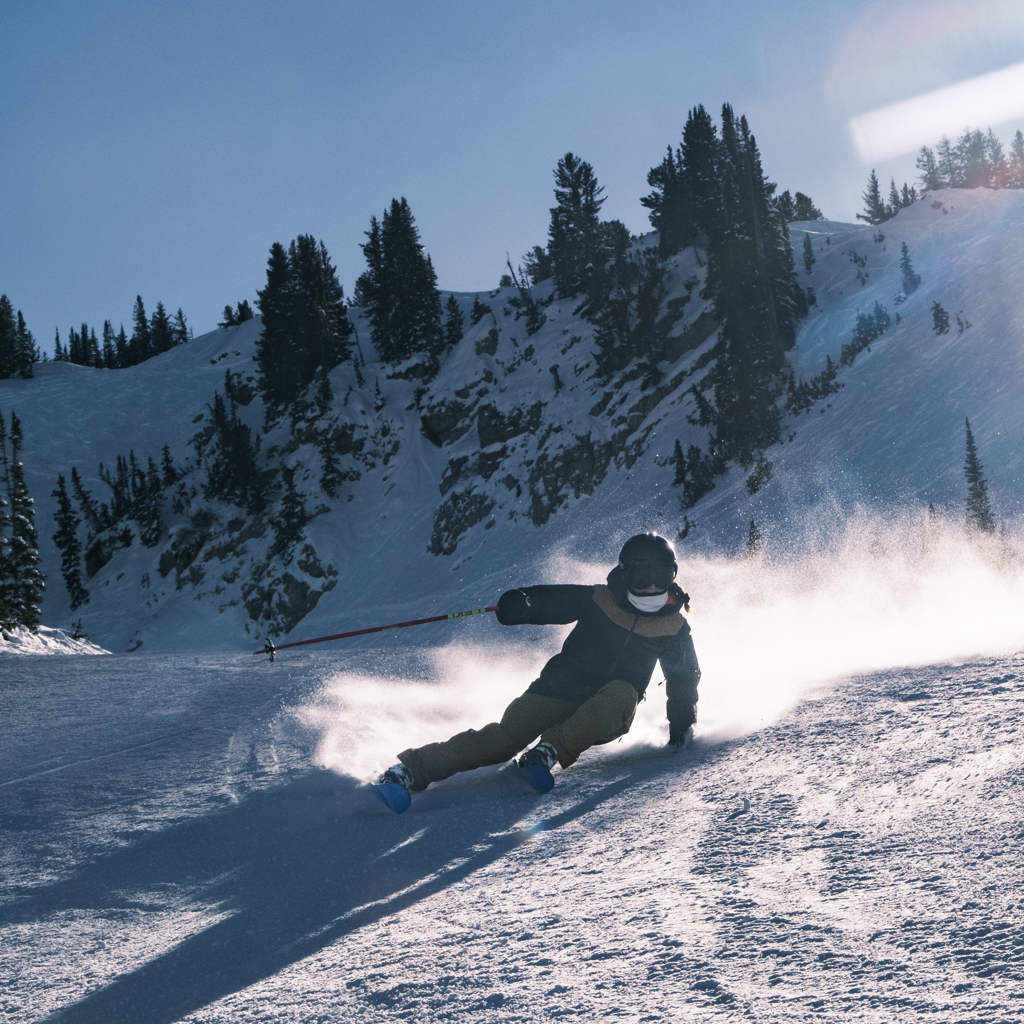 A skier in a Norrøna jacket skis down a snowy mountainside, with the sun shining brightly in the background. 

