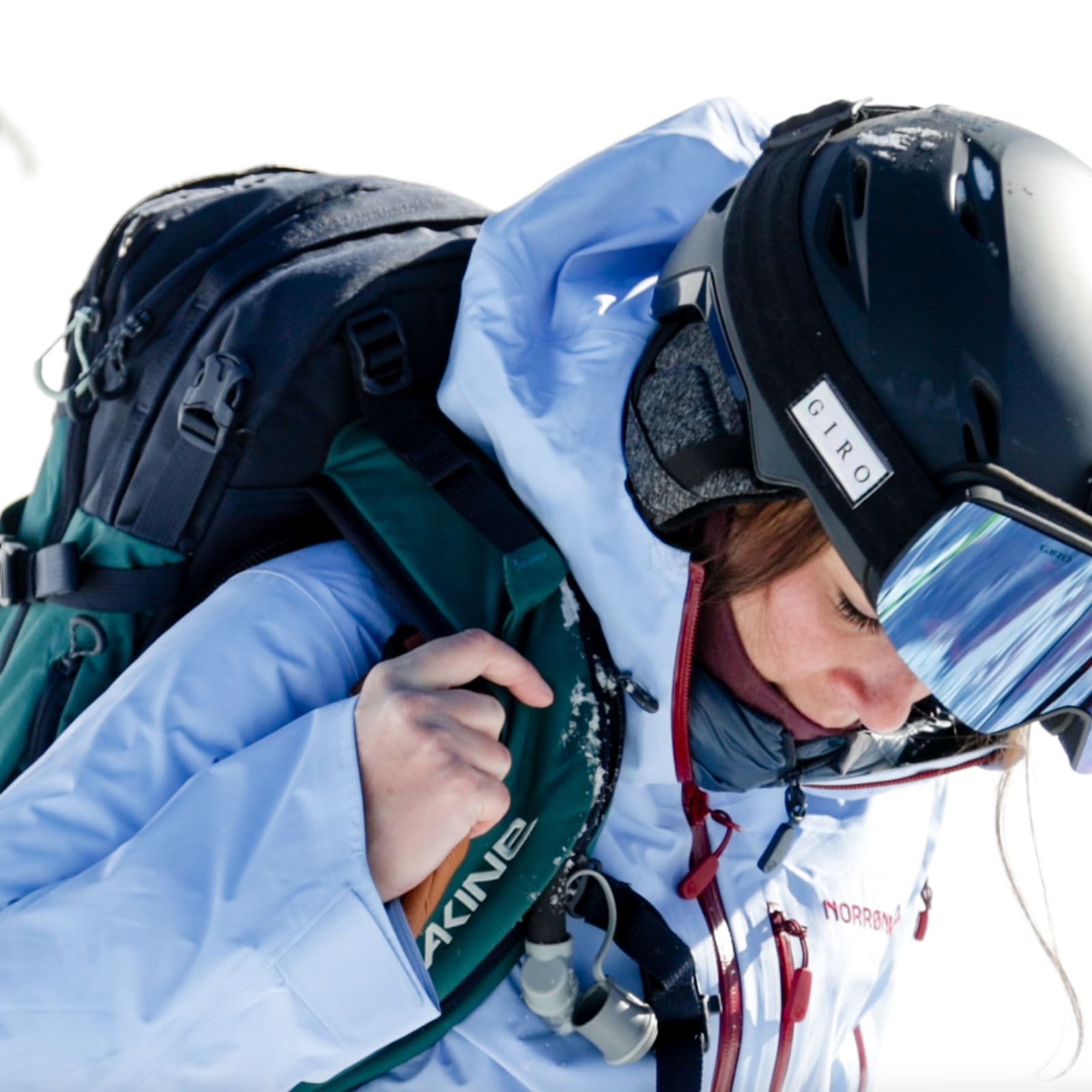Close-up of a skier with Giro helmet and goggles, wearing a blue Norrøna jacket and a Dakine backpack, on a snowy field.