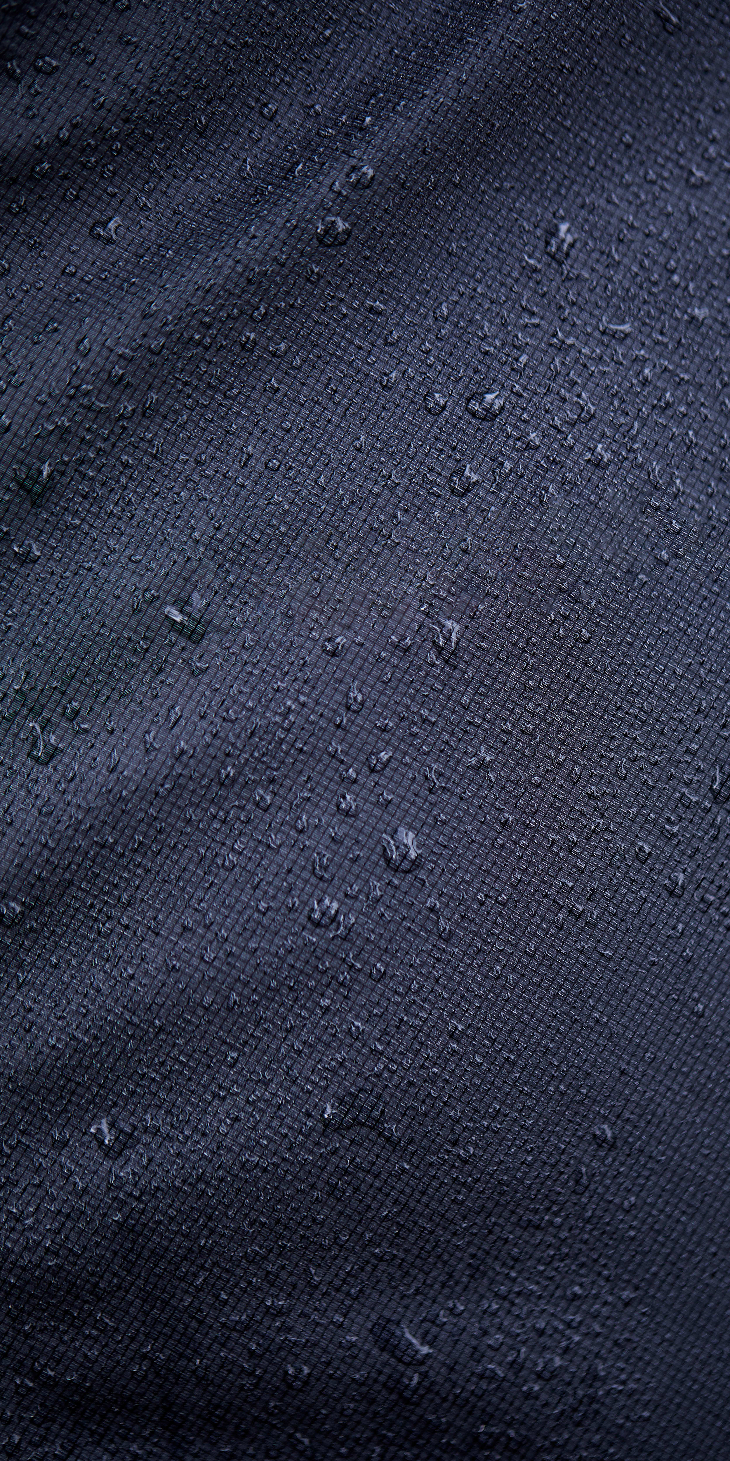 Close-up of water droplets on a dark, textured Norrøna fabric. 
