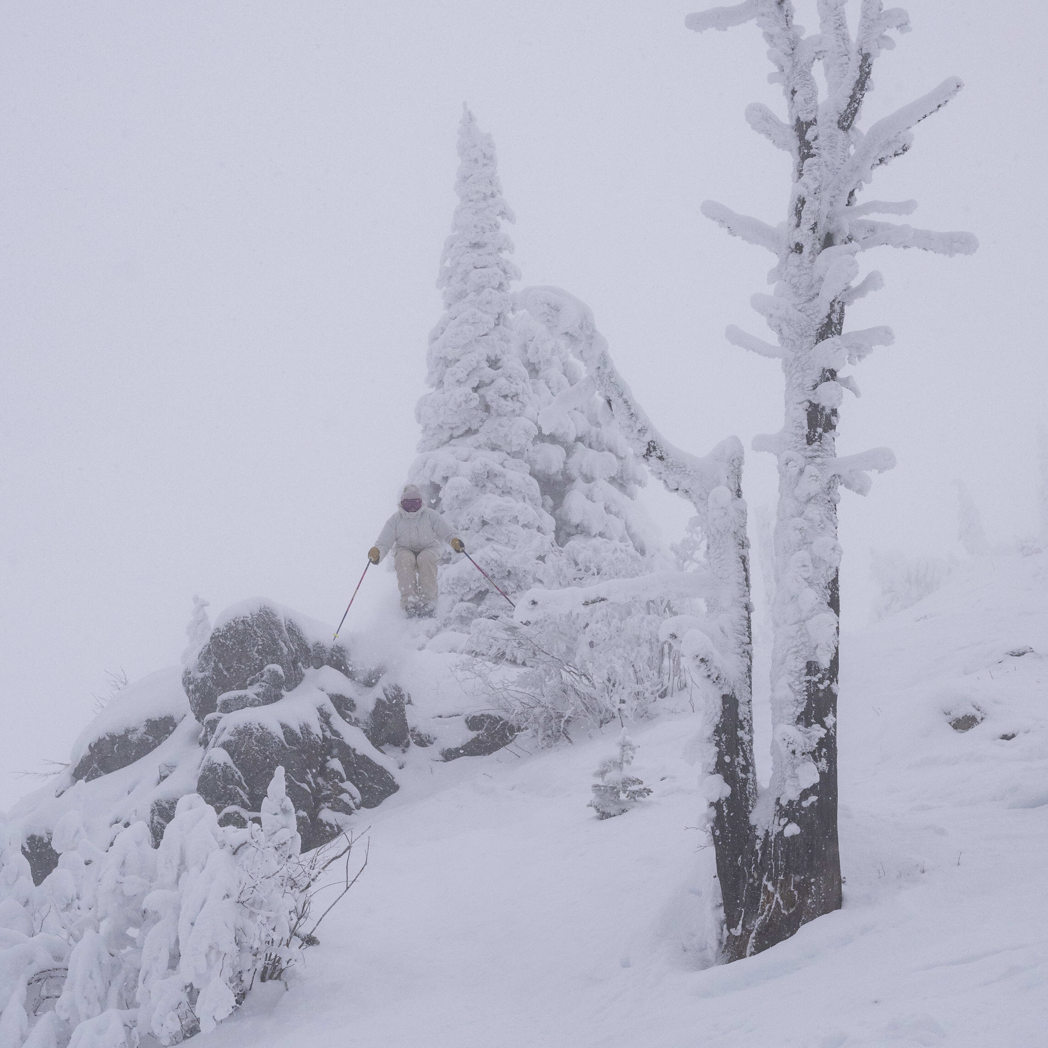 A person wearing a Norrøna jacket skis down a snowy mountain slope.