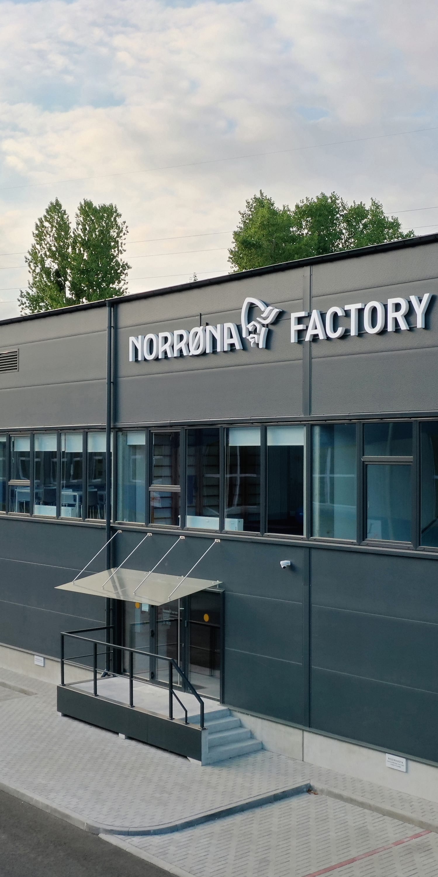 Norrøna Factory building with a gray exterior, multiple windows, and a paved entrance.  
