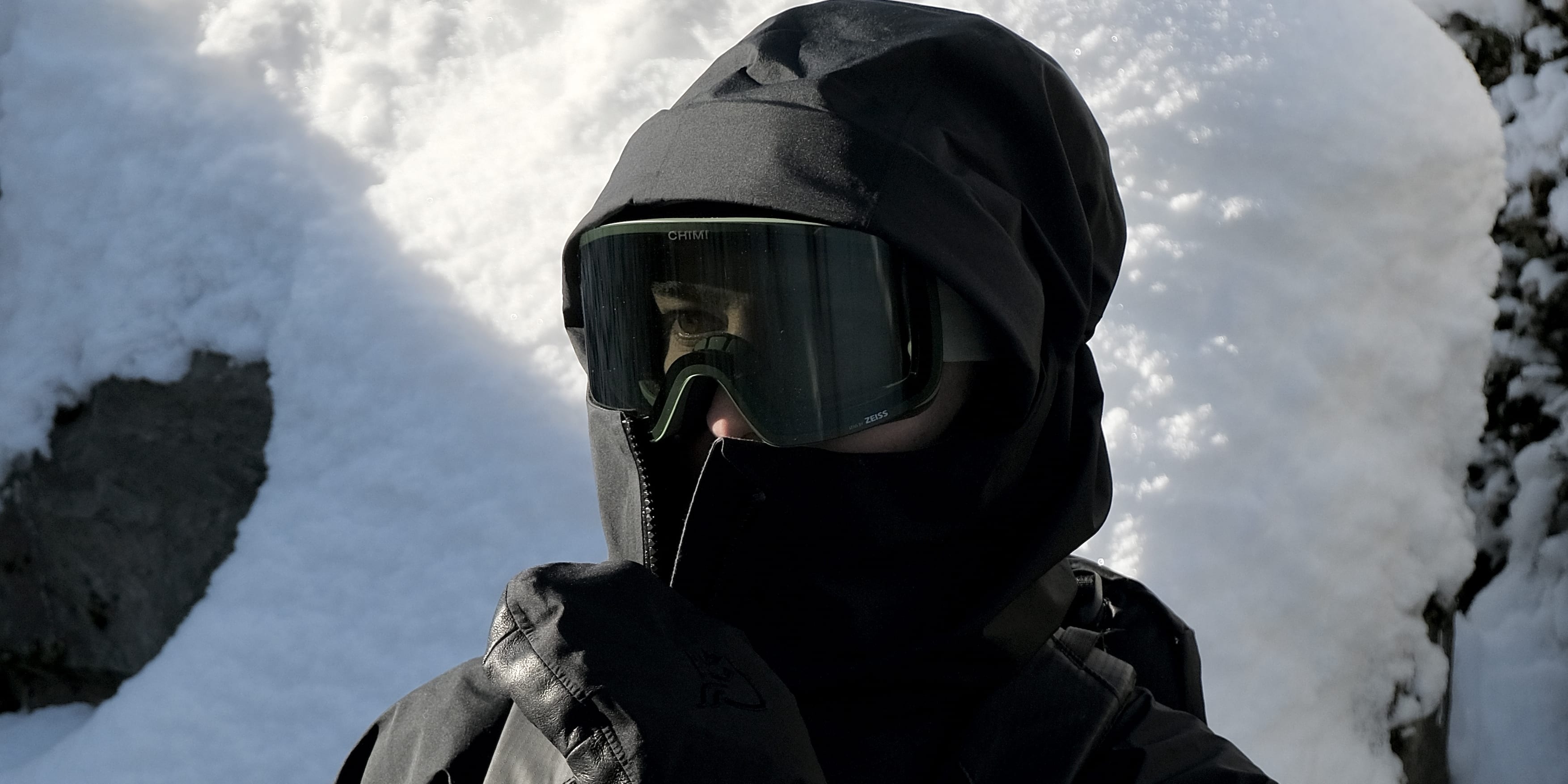 Person wearing a Norrøna jacket, gloves, and ski goggles, holding two ski poles, standing in snow. 

