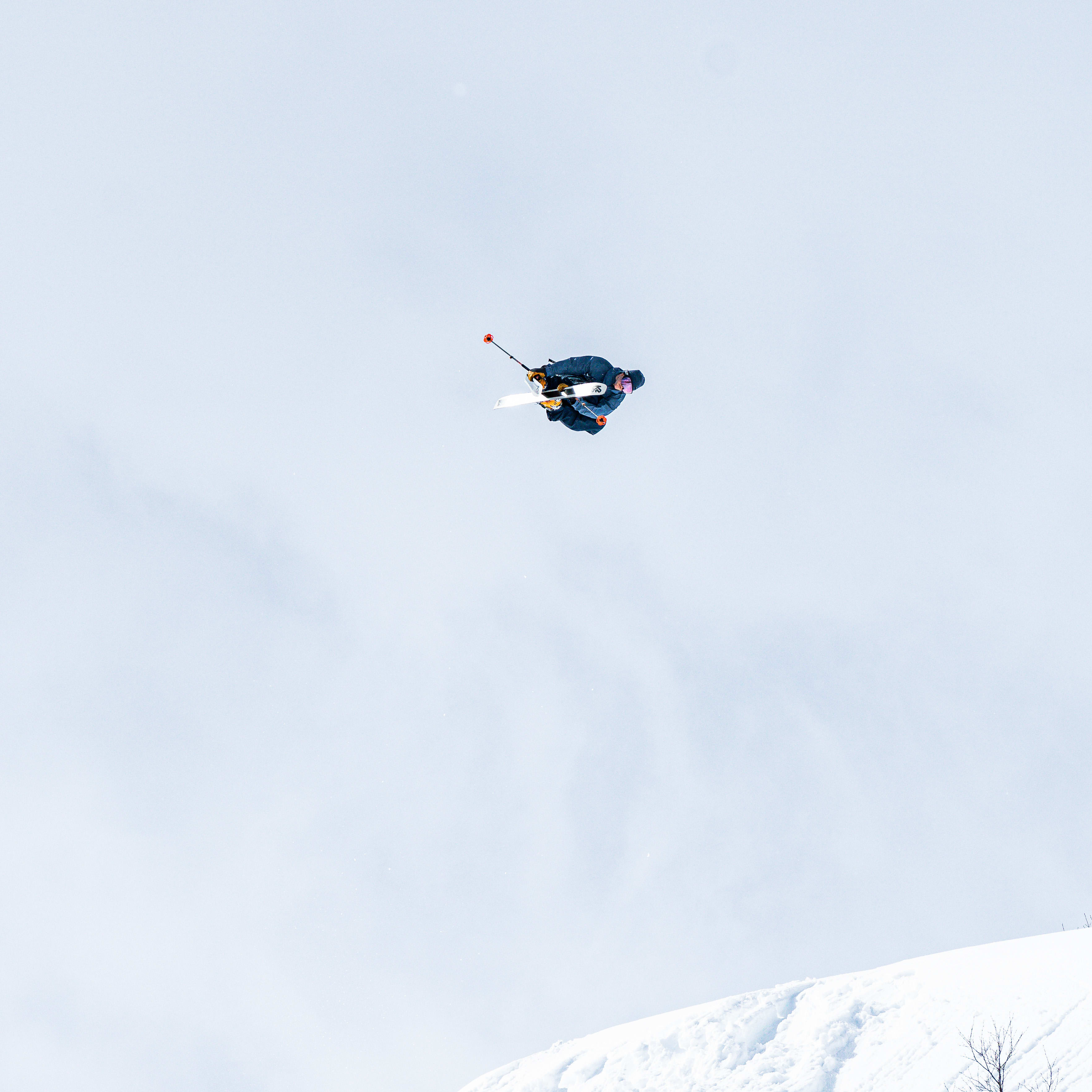 A skier wearing Norrøna clothing performs a backflip off a snowy mountain peak.