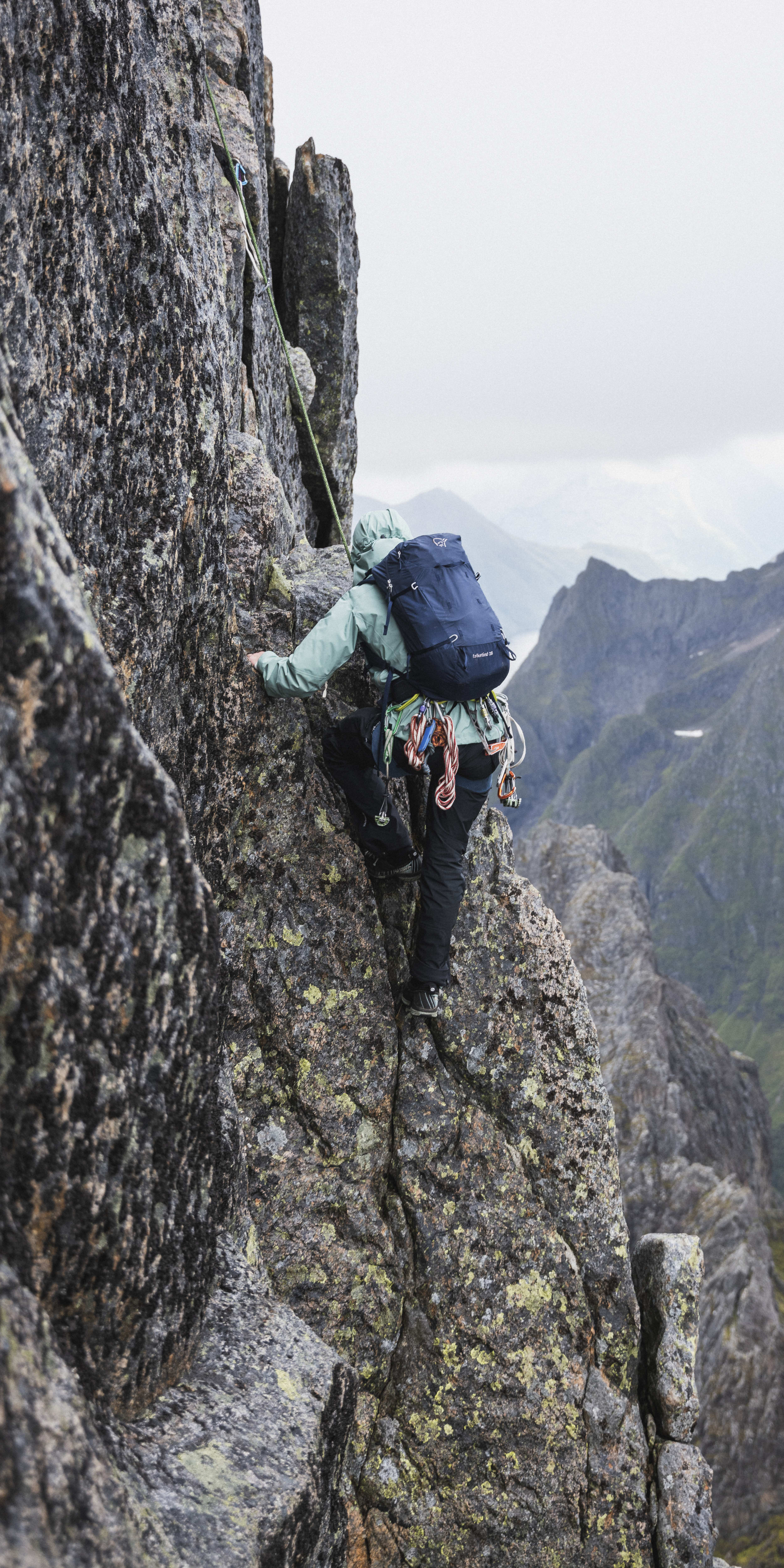 A person wearing a Norrøna backpack climbs a rocky mountainside.  
