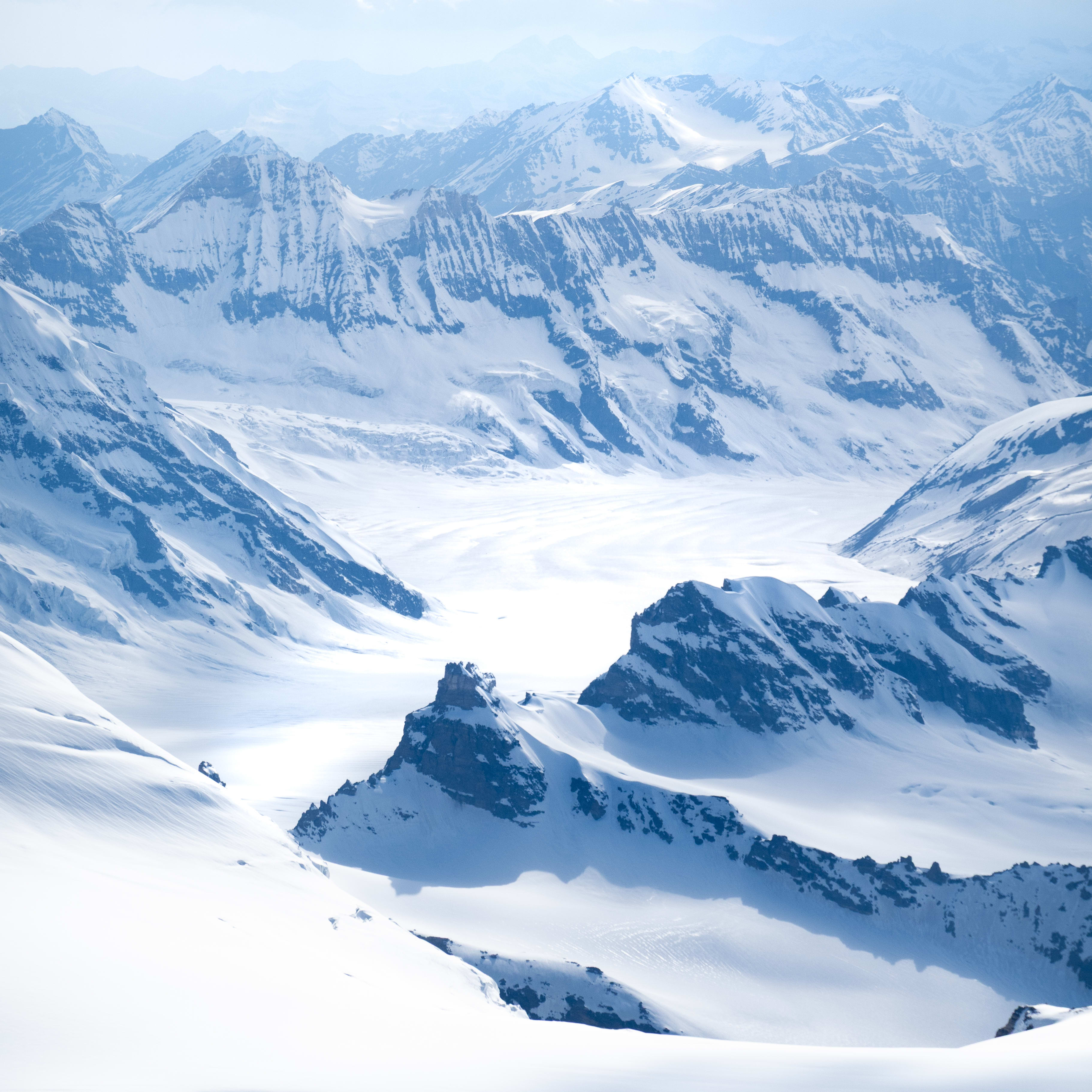 Aerial view of snow covered mountains with clouds in the background.