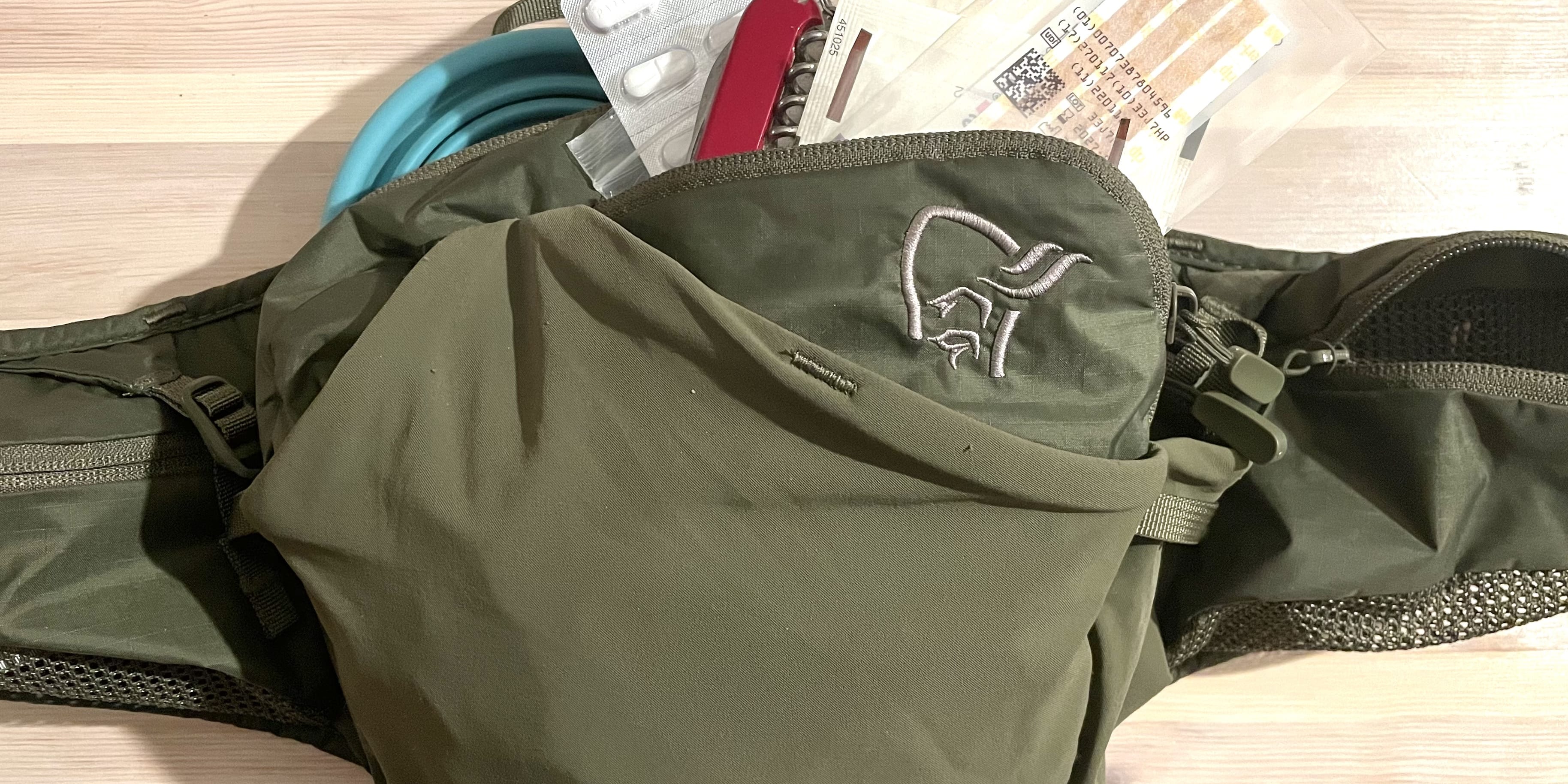 A green fanny pack with a zippered pocket, a mesh pocket, a black strap and a small gray logo.