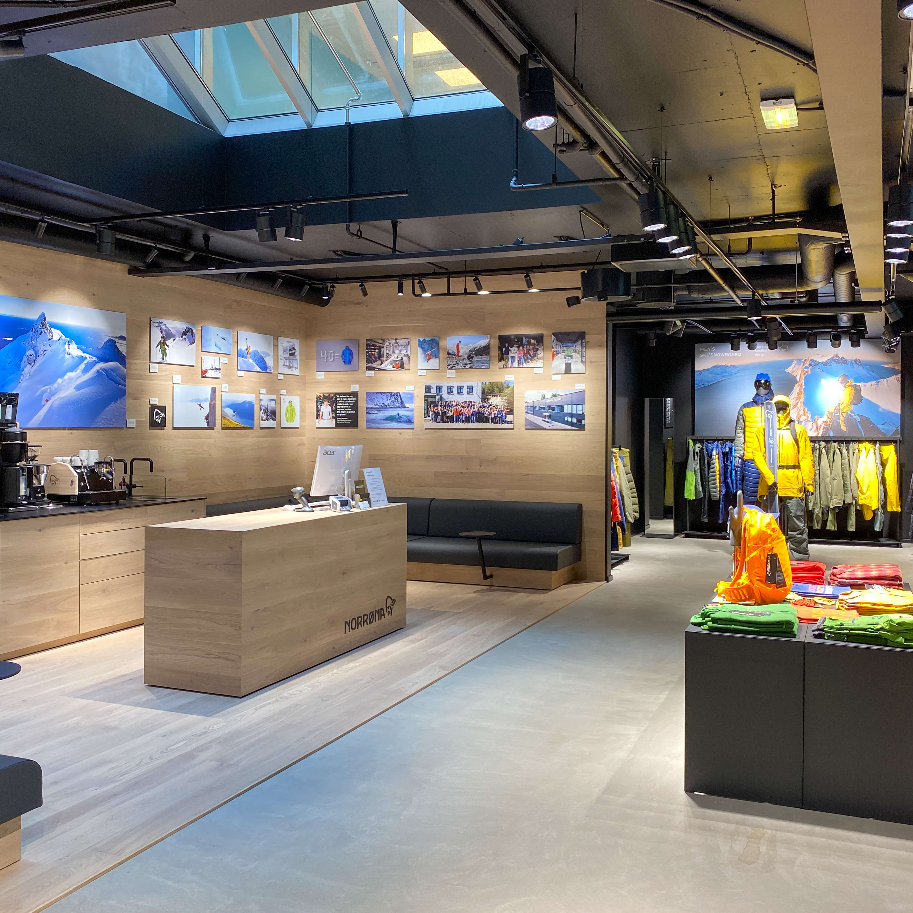 A Norrøna store interior with wood floors, a black couch, and a display of Norrøna clothing on mannequins.