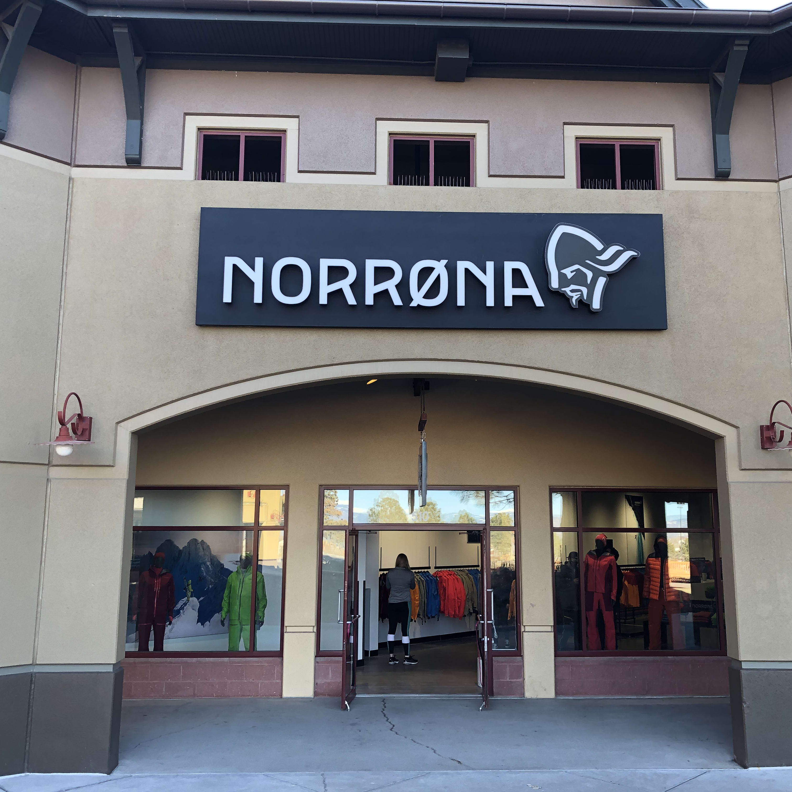 A storefront for the Norrøna outdoor clothing brand, featuring a large sign with the company's logo. The store windows display mannequins wearing Norrøna clothing.