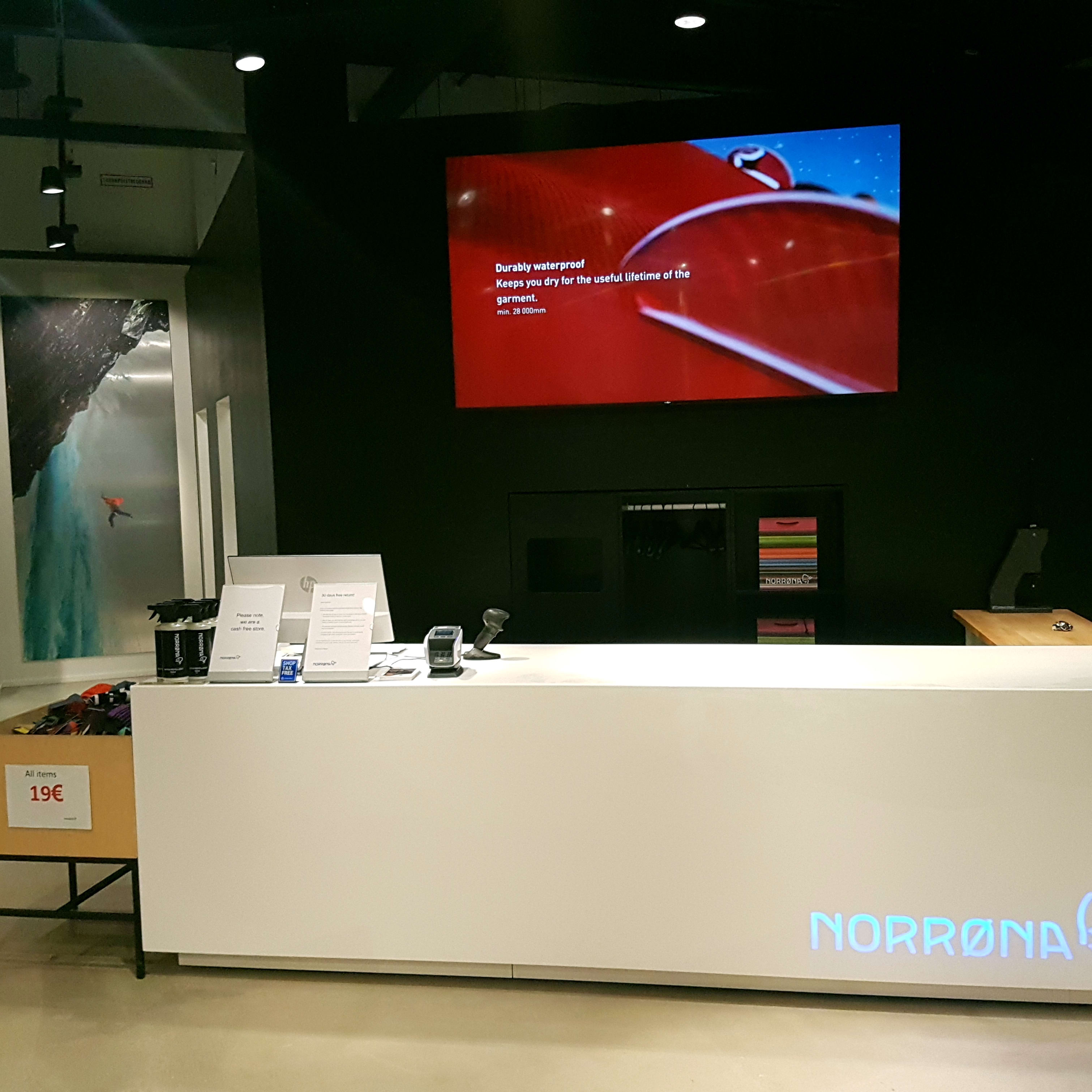 Norrøna store checkout counter with a large display screen and a mannequin wearing an orange Norrøna jacket.