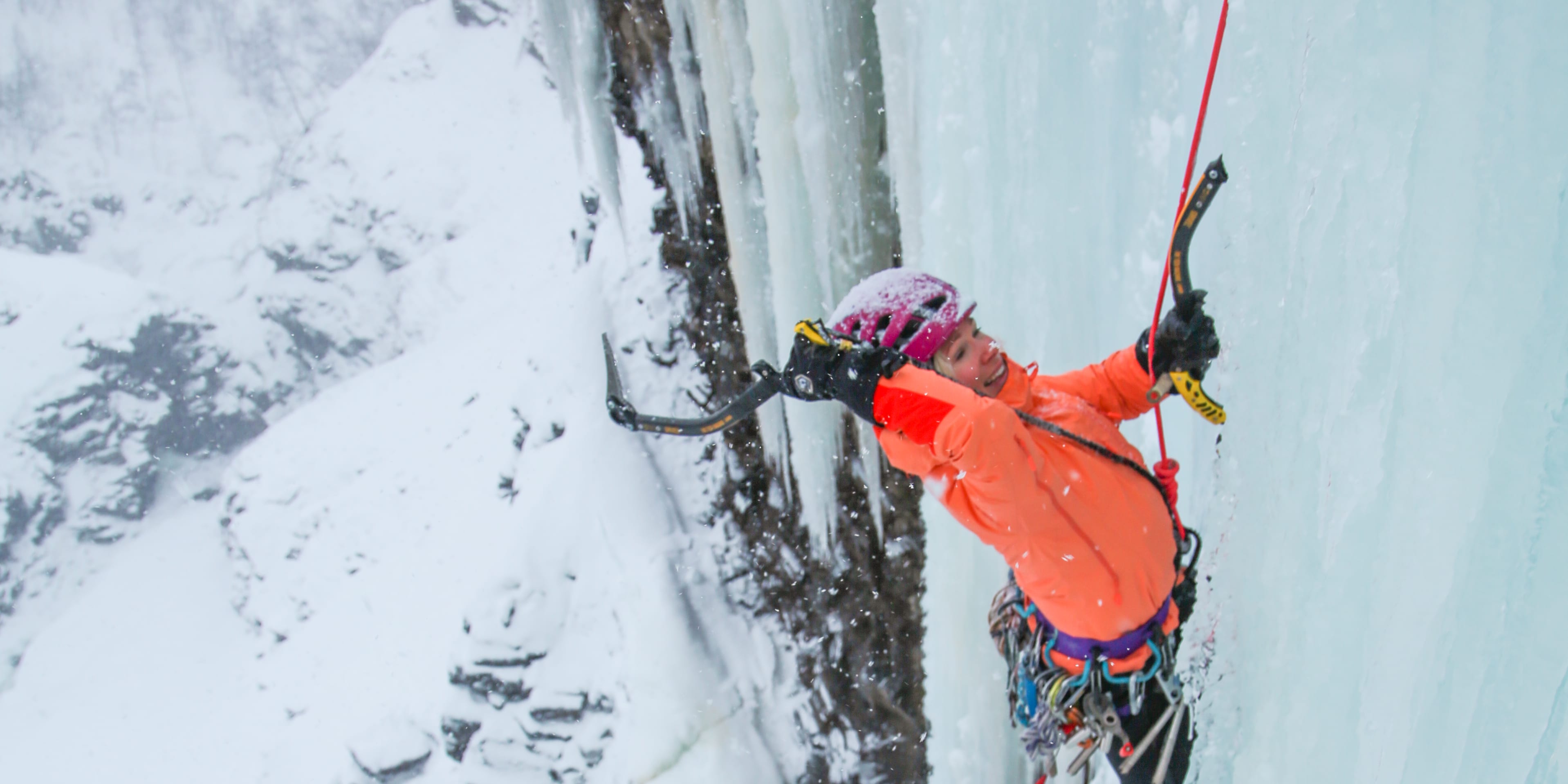 A climber wearing a Norrøna jacket and helmet ice climbs a frozen waterfall. 
