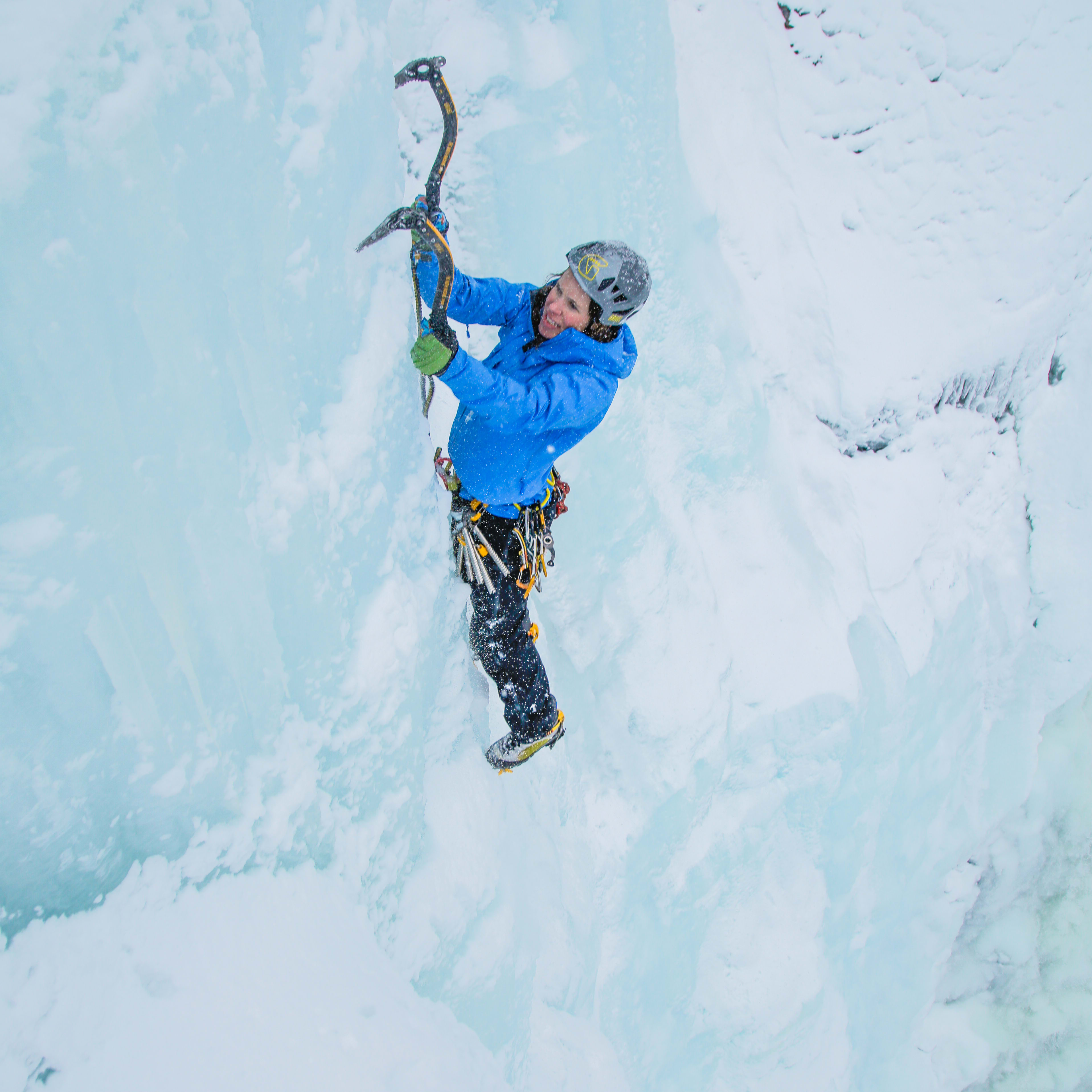 A man wearing a Norrøna jacket ice climbs a frozen waterfall. 
