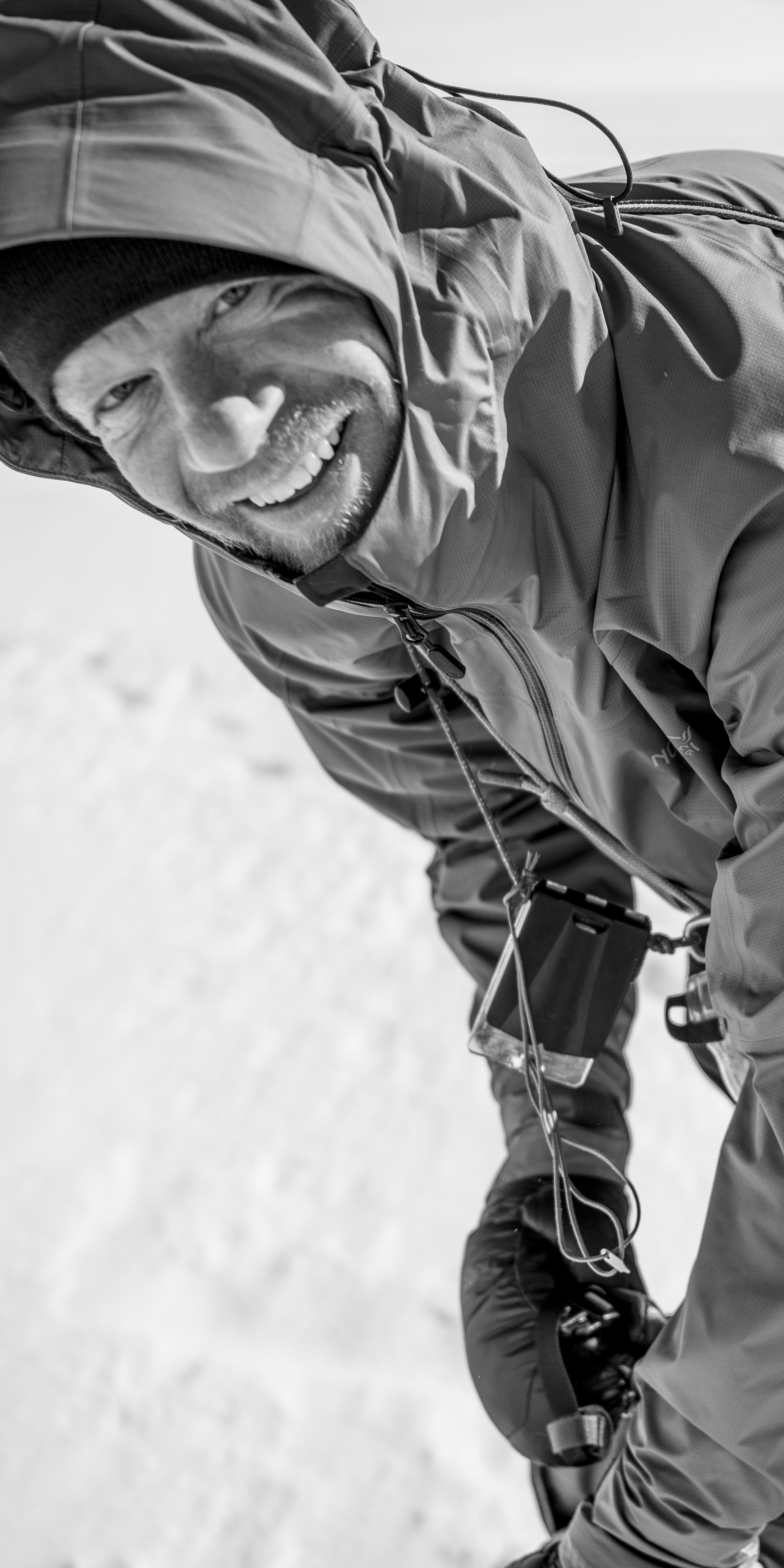A man wearing a Norrøna jacket smiles as he looks at a map in a clear plastic case. 
