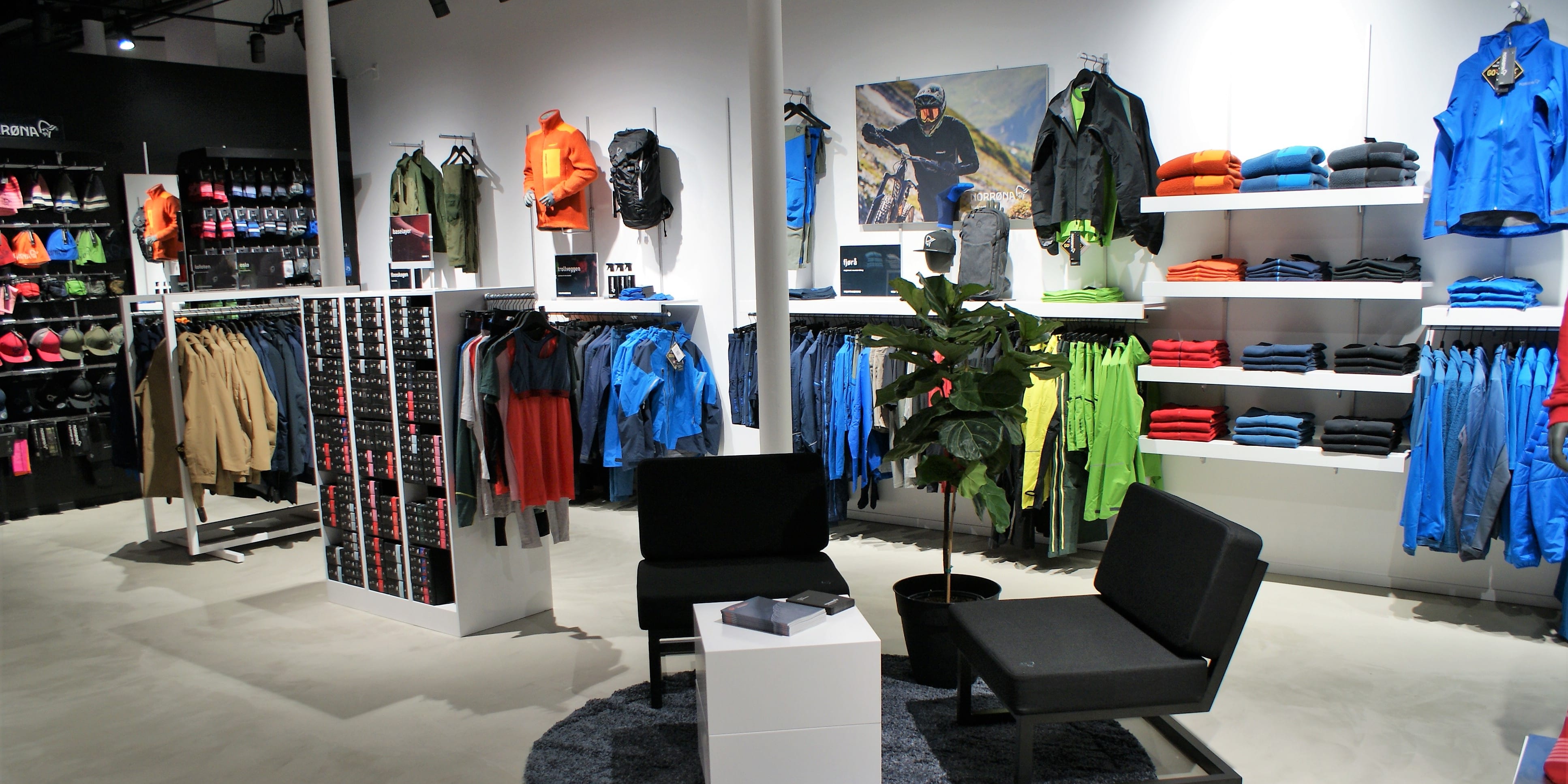 A Norrøna clothing store with a display of clothing, accessories, and a plant.  The floor is concrete.  The store is lit with track lighting.