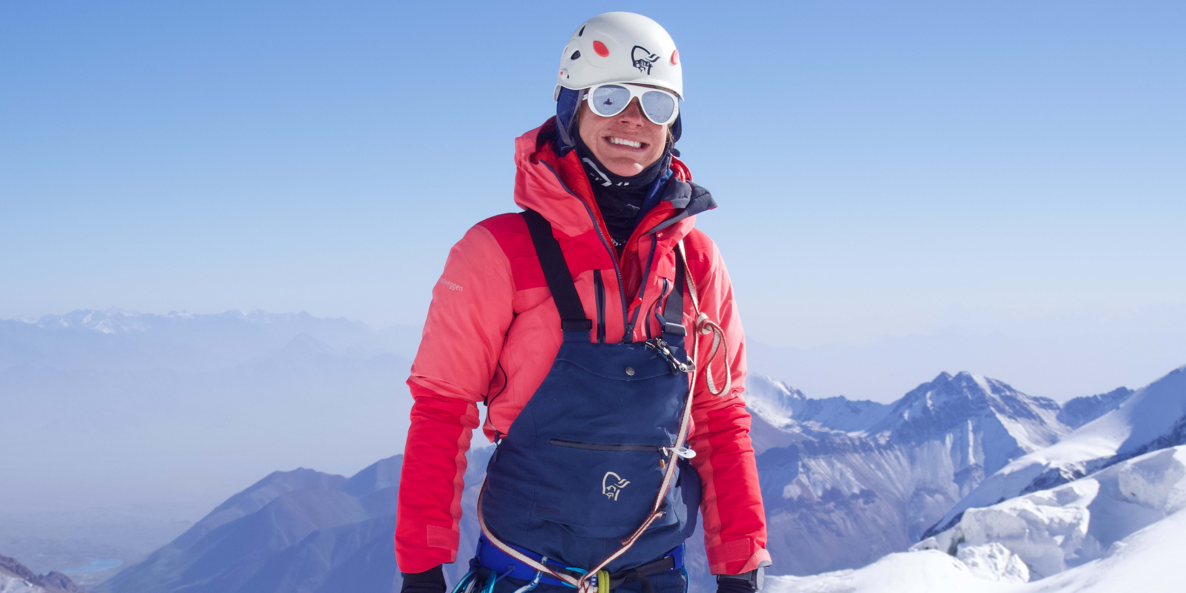 A climber in red and blue Norrøna gear smiles on a snowy mountain summit.