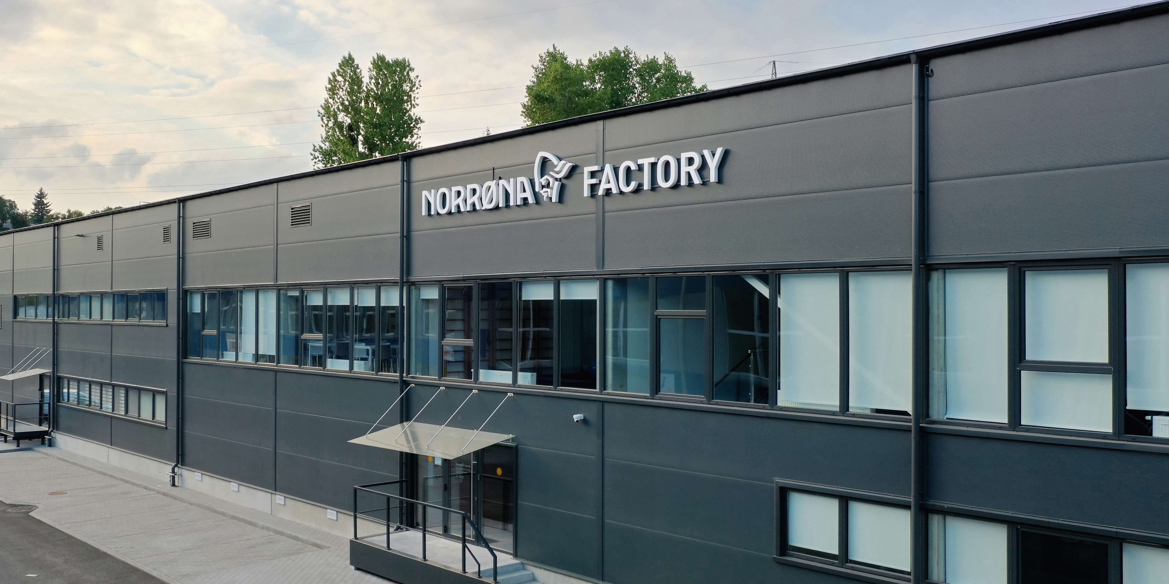Norrøna Factory building with a gray exterior, multiple windows, and a paved entrance.  
