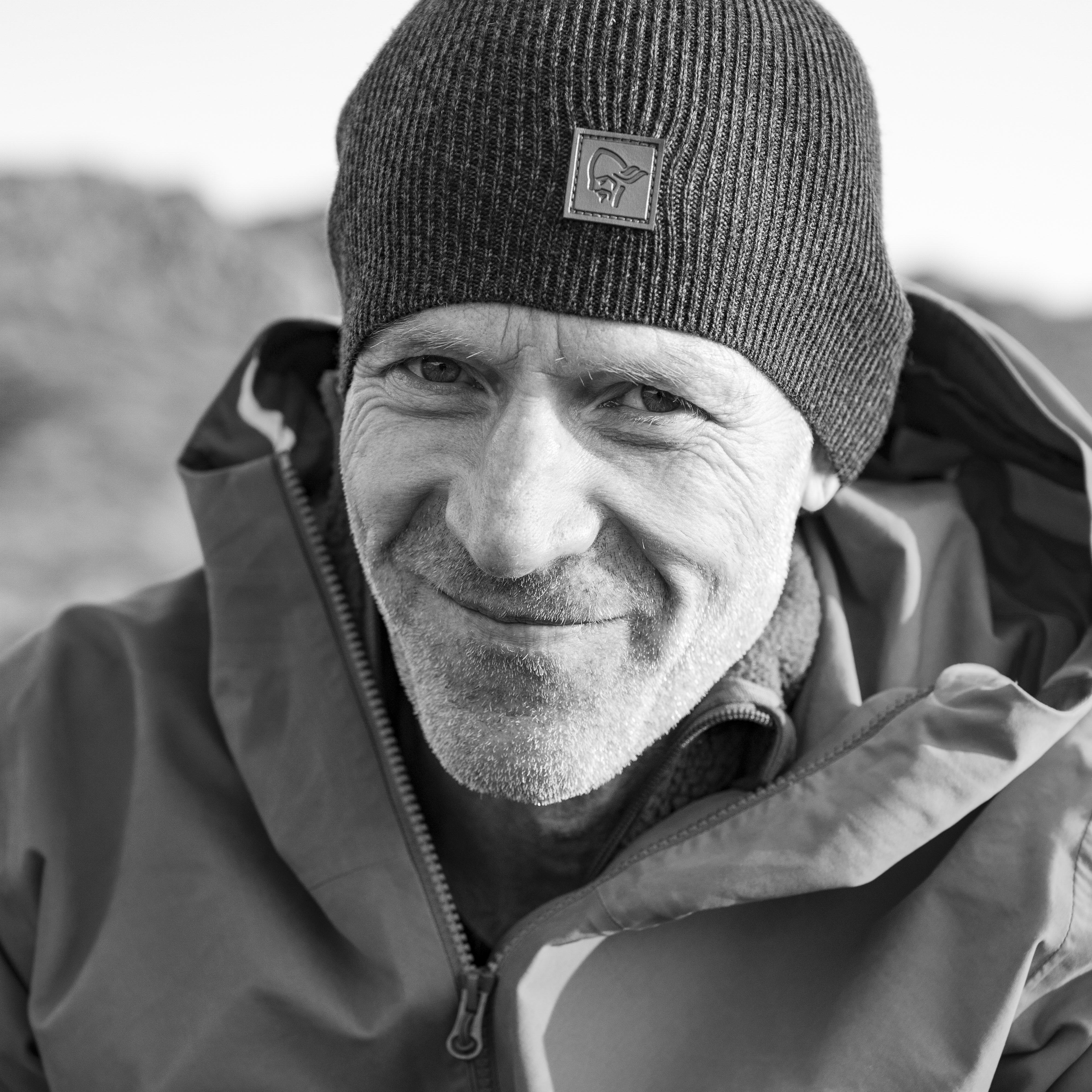 A man wearing a Norrøna beanie and jacket, smiling at the camera.