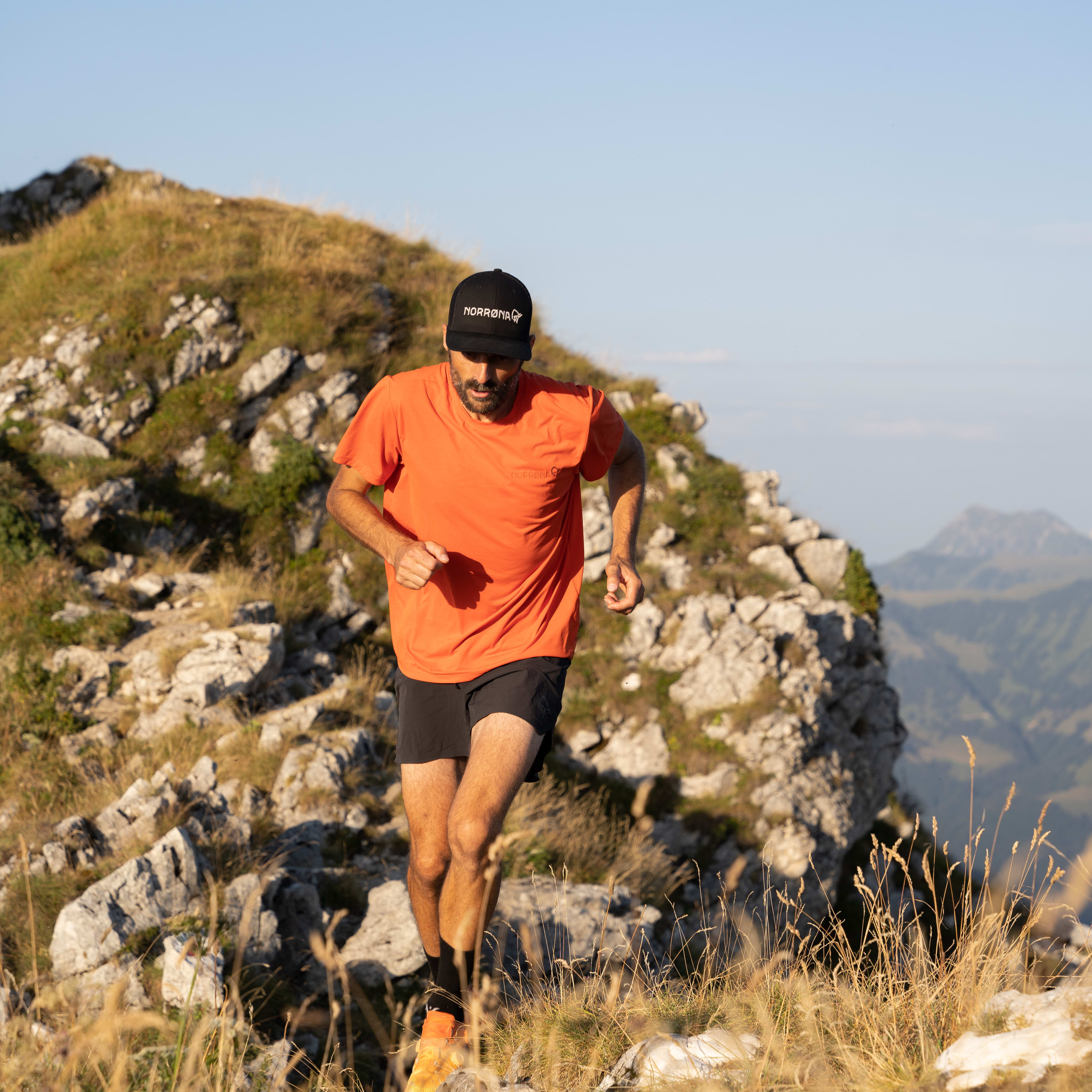 A man in a Norrøna cap and shirt runs up a rocky hillside. 
