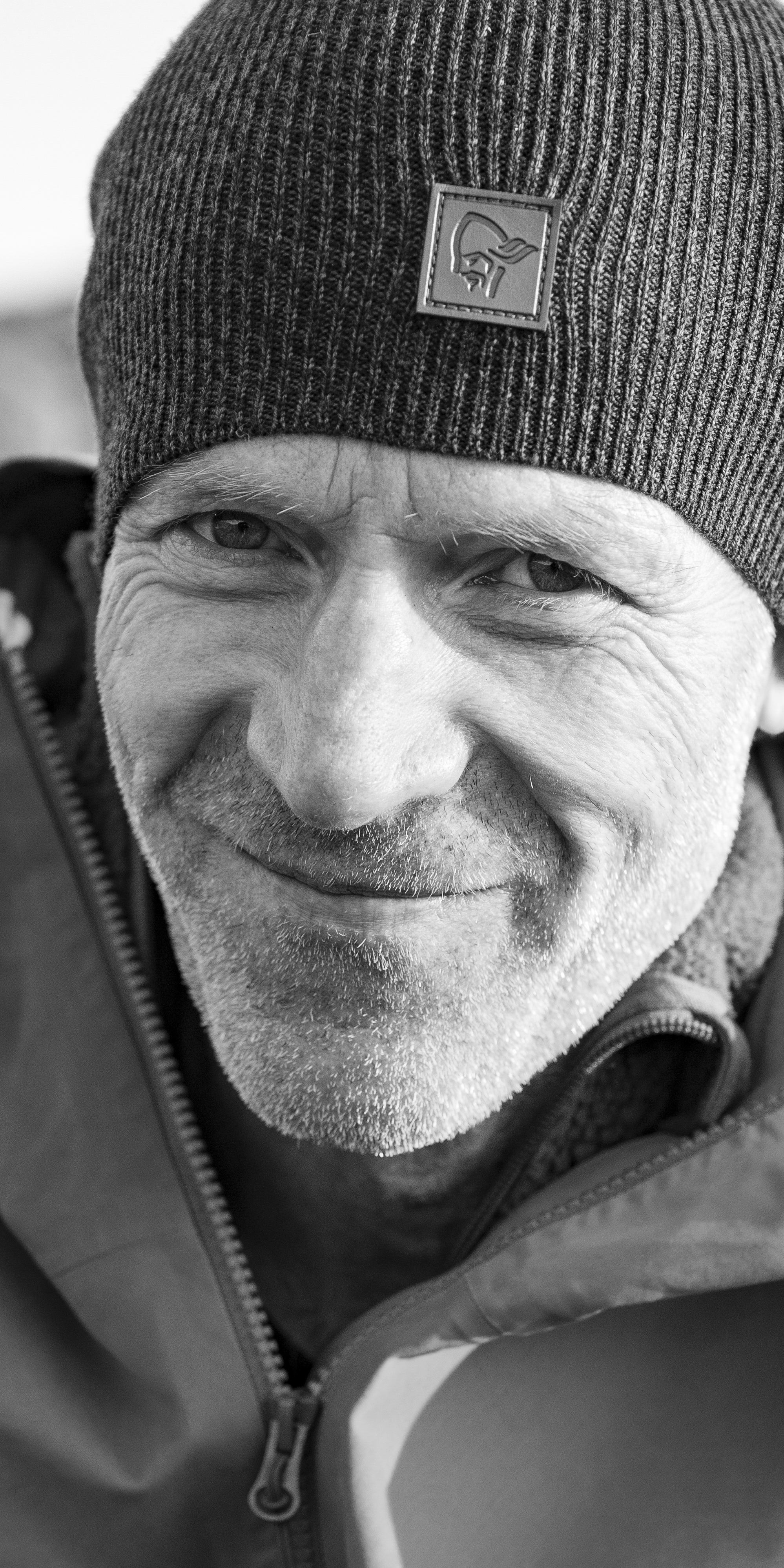 A man wearing a Norrøna beanie and jacket, smiling at the camera.  
