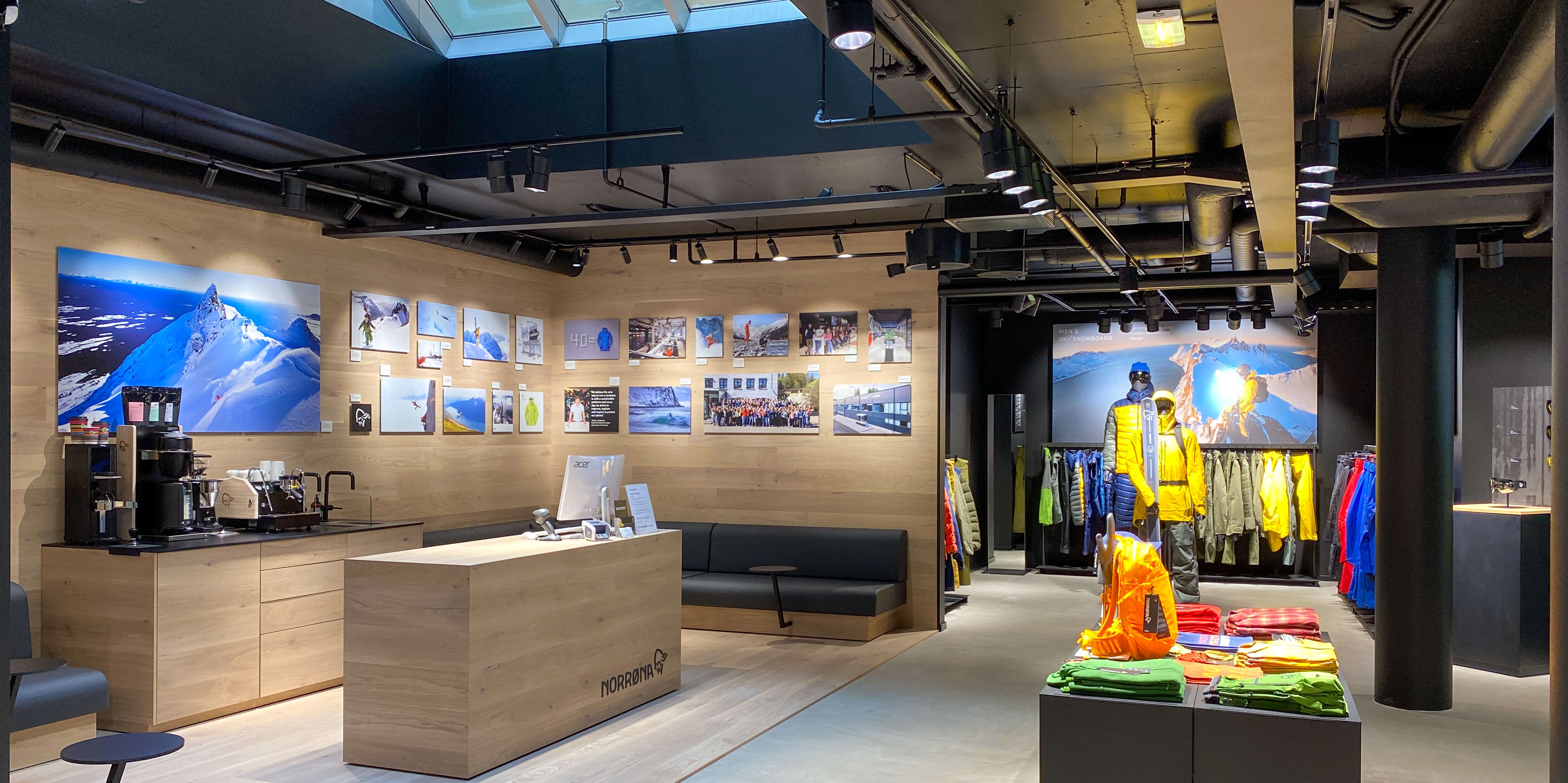 A Norrøna store interior with wood floors, a black couch, and a display of Norrøna clothing on mannequins. 
