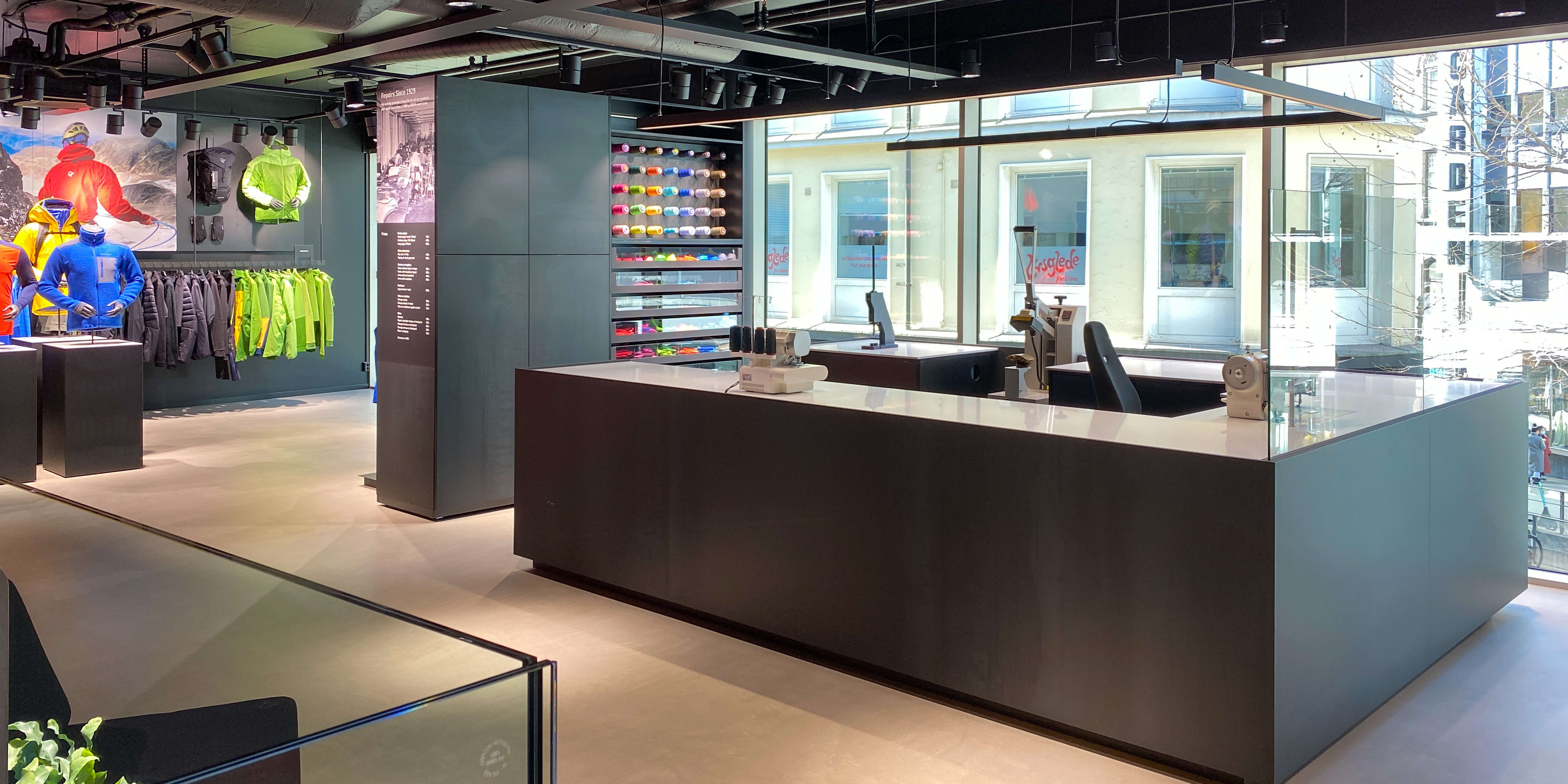 A modern retail space with a black counter, displaying Norrøna clothing on mannequins and a shelf of colorful spools of thread. 
