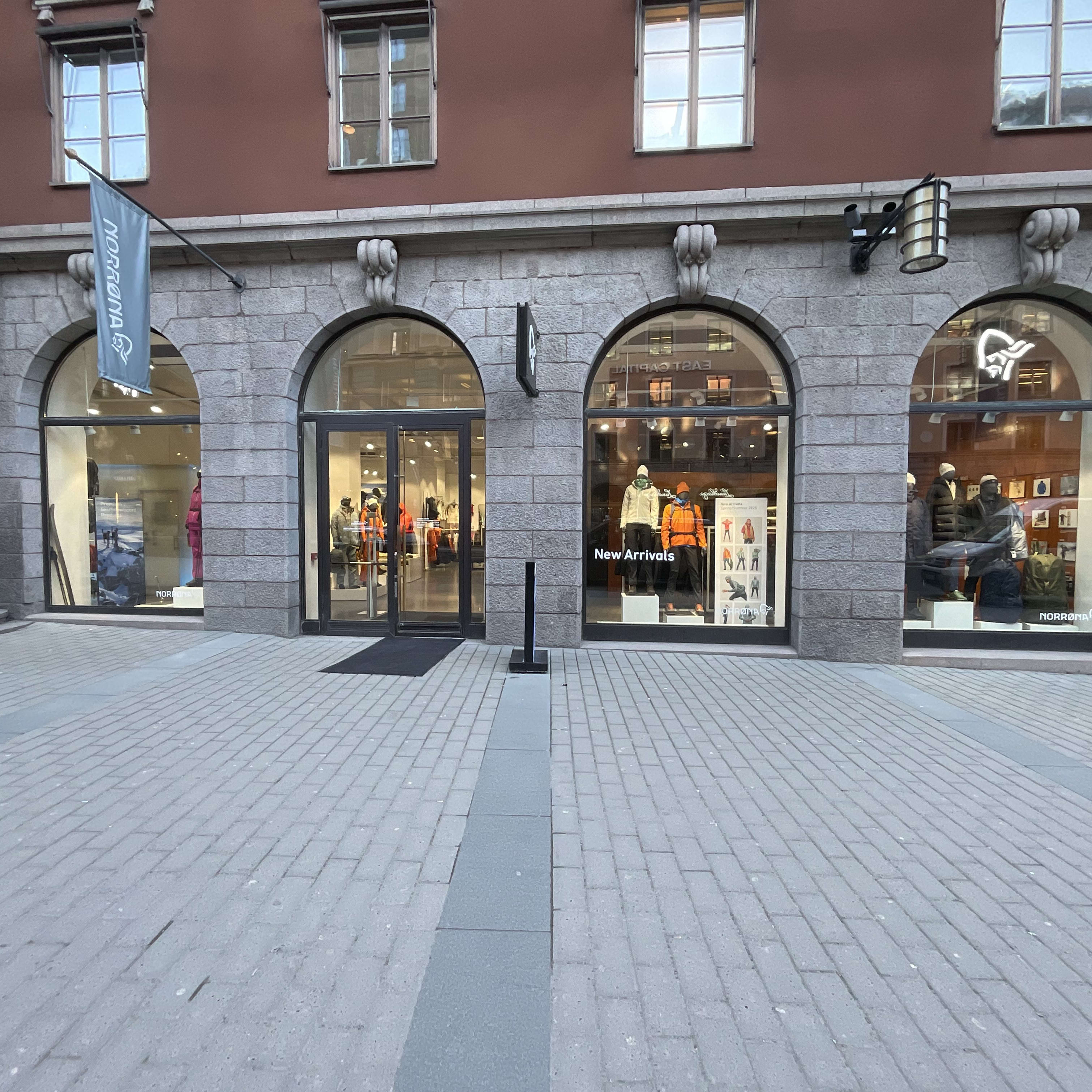 A Norrøna storefront with a large arched window displaying mannequins wearing outdoor clothing. The sign reads "New Arrivals." 
