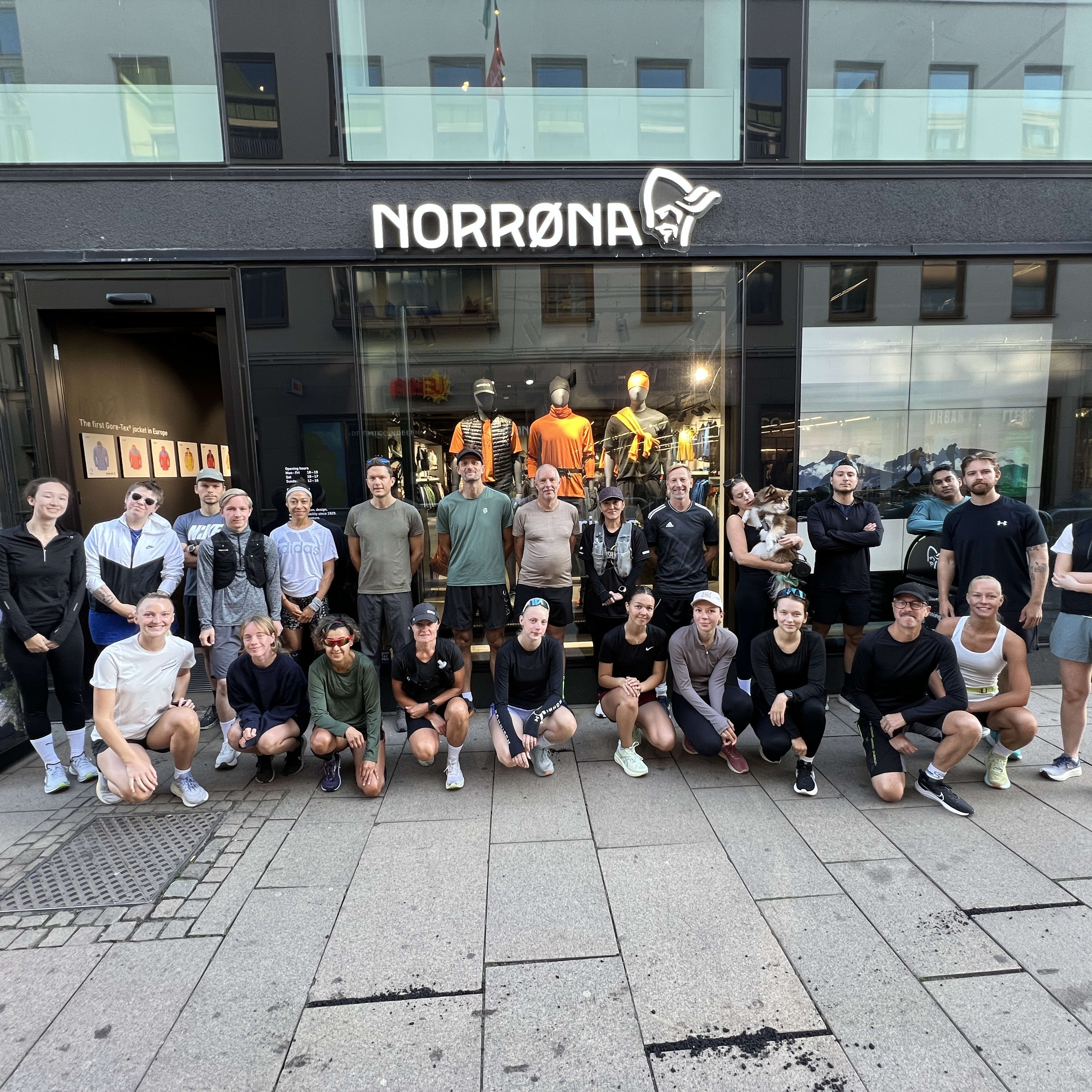 Group of people, wearing athletic clothes, posing in front of a Norrøna store. Some Norrøna brand clothing is visible.