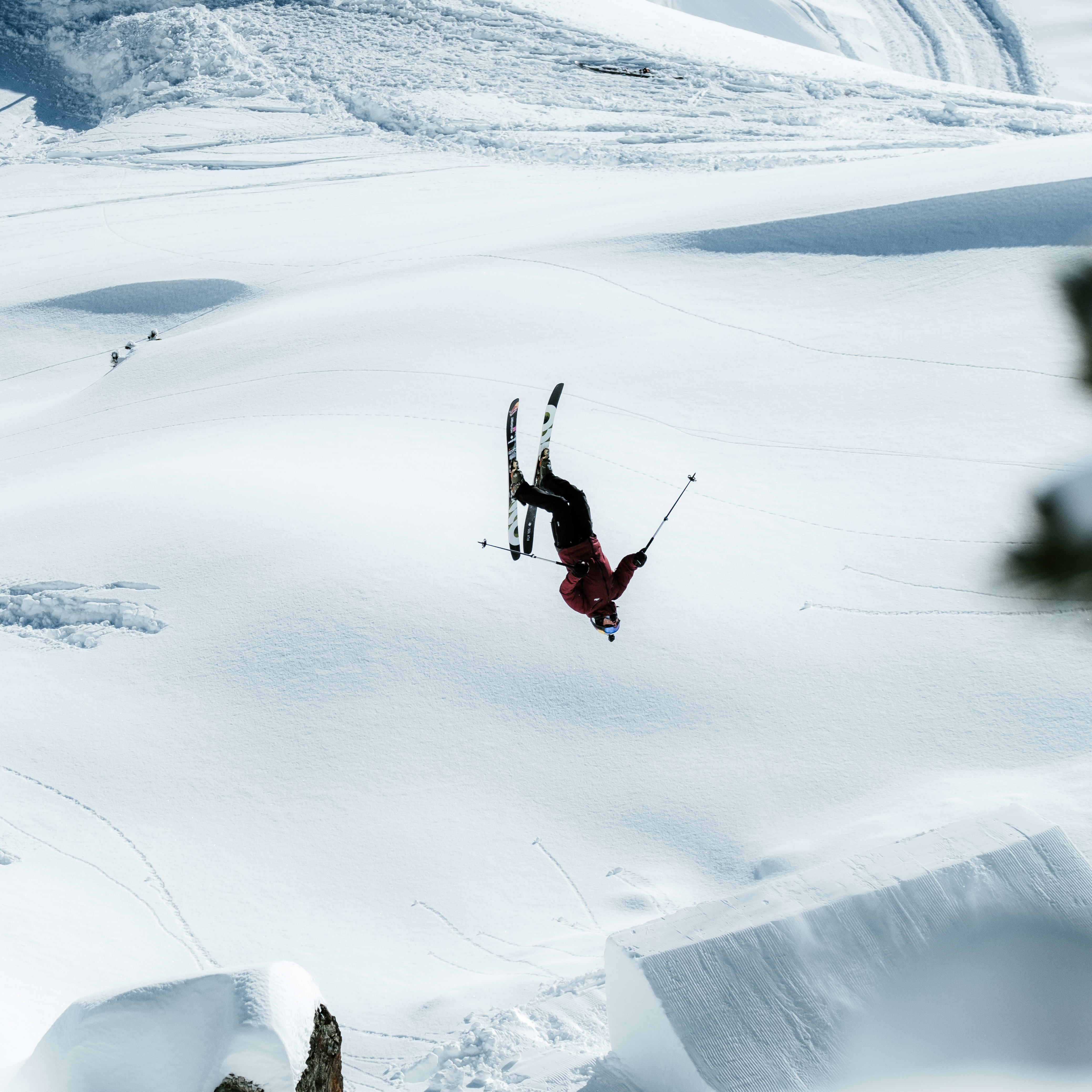 A skier wearing a Norrøna jacket performs an inverted trick over a snow-covered terrain.