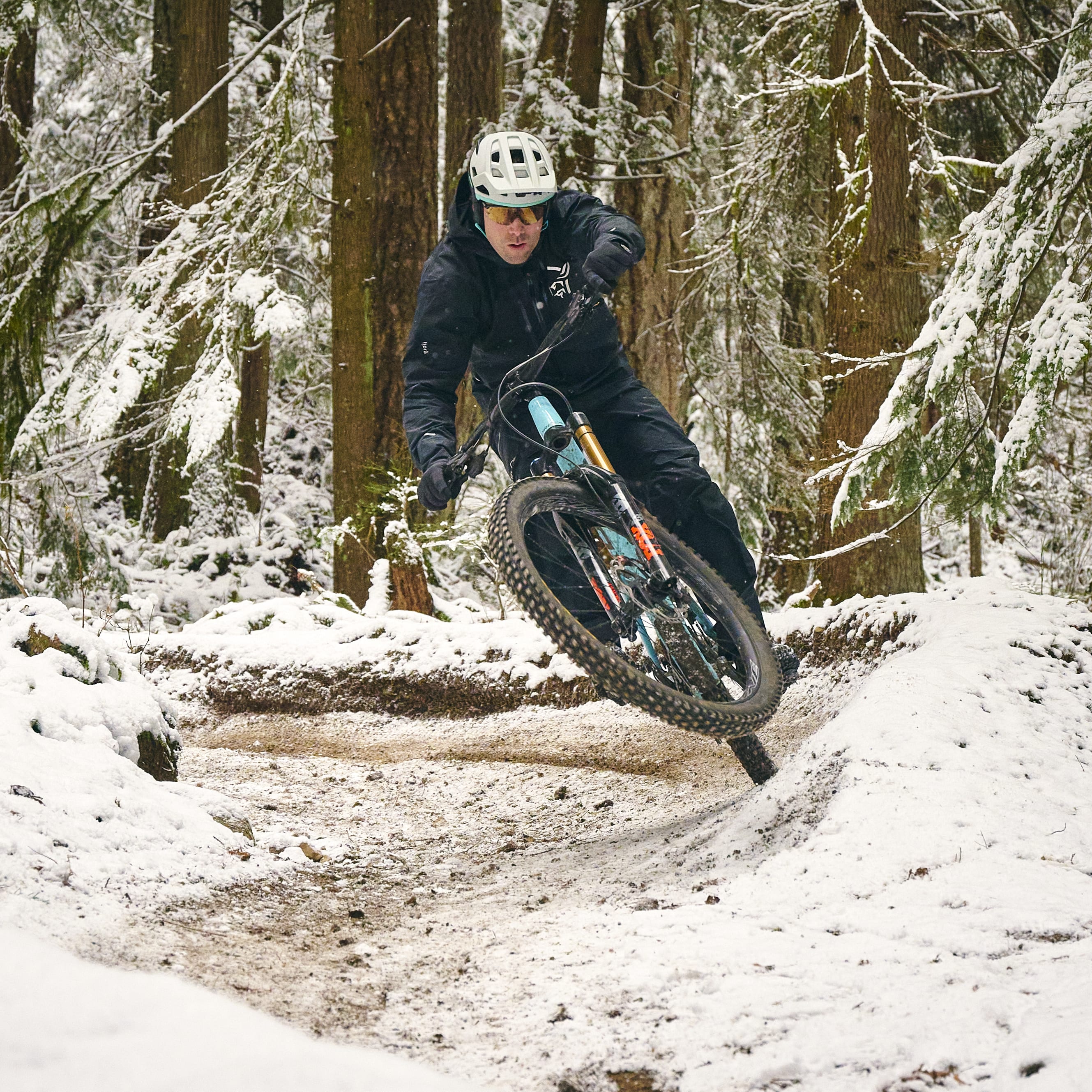 A person in a Norrøna jacket rides a mountain bike on a snowy trail.