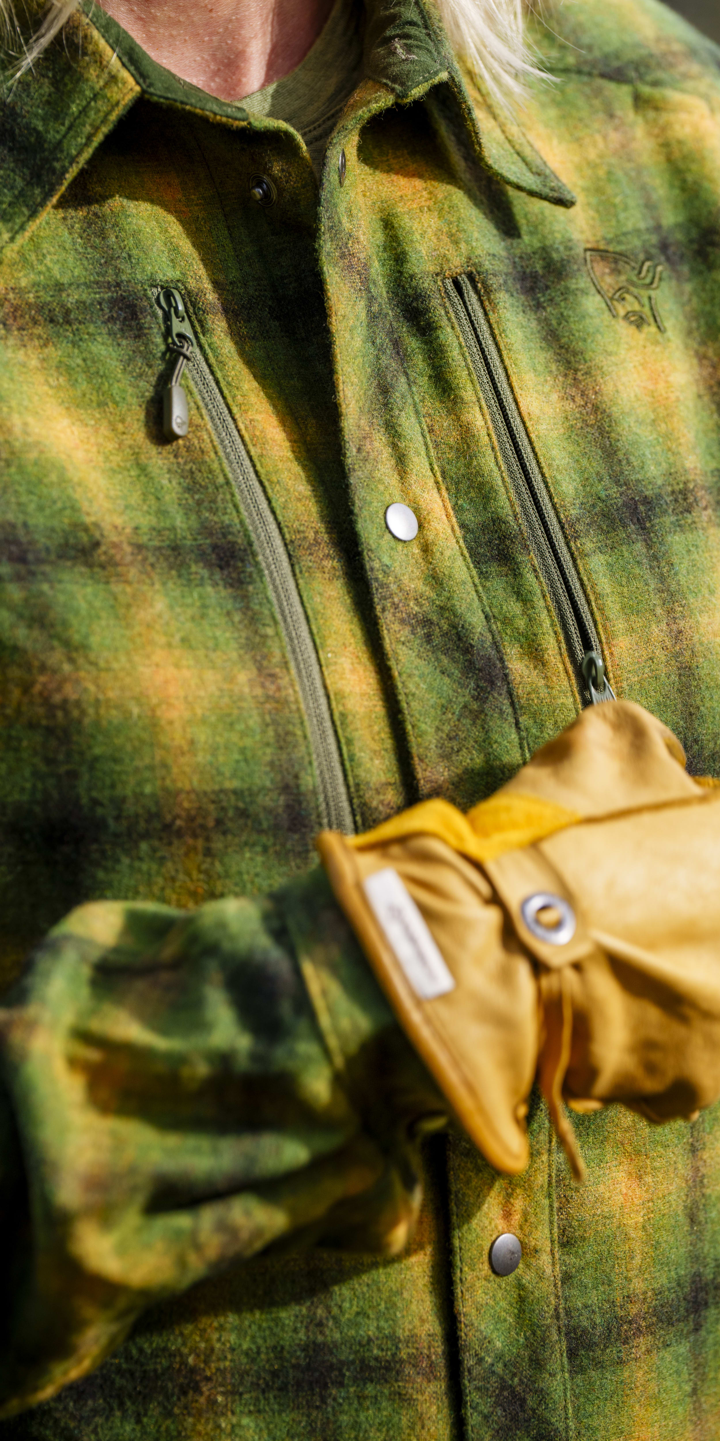 Closeup of a green, yellow, and black plaid Norrøna shirt with a tan leather glove on one sleeve. 
