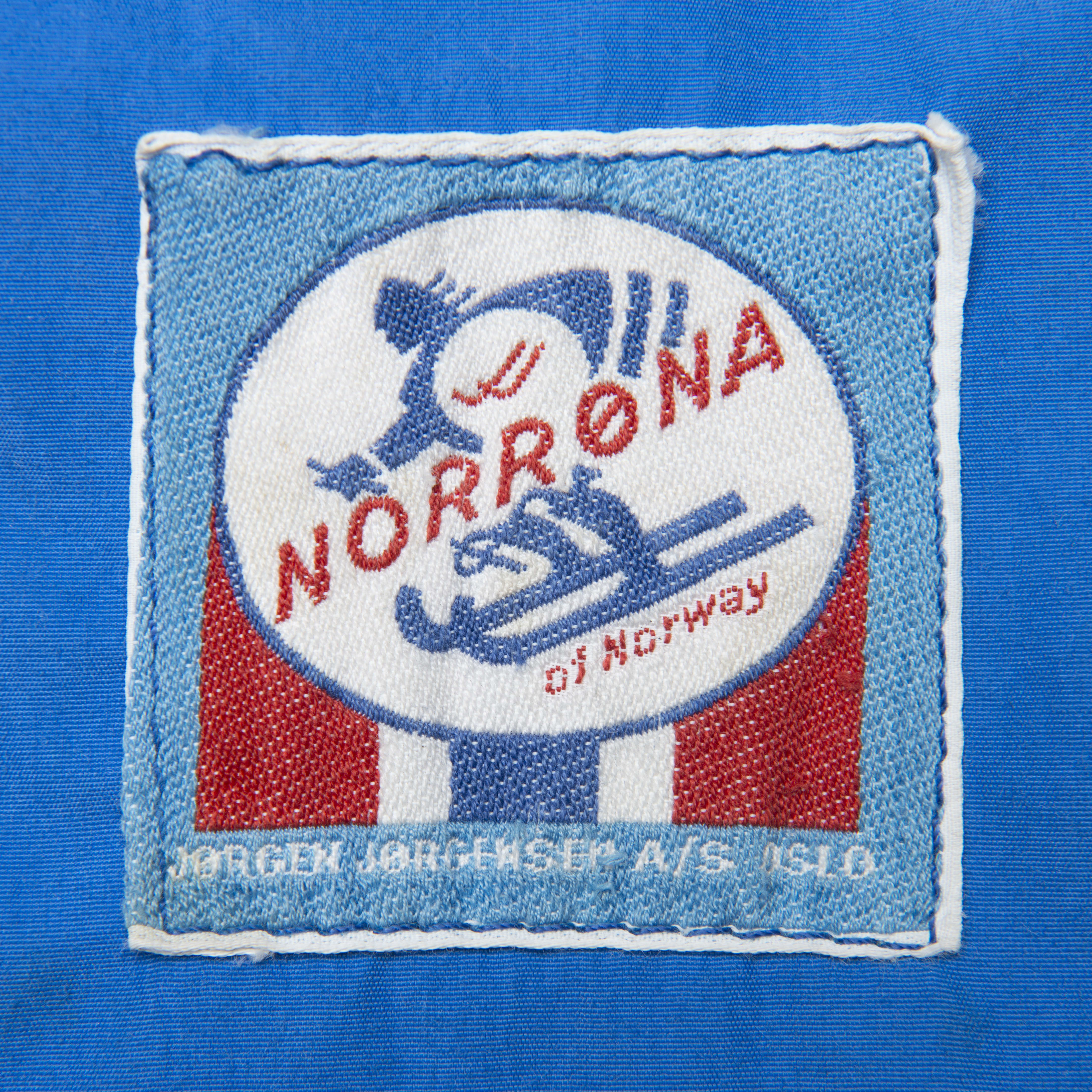 Norrøna patch on blue fabric. Patch depicts a skier, the Norrøna logo, and the text "Jørgen Jørgensen A/S Oslo".
