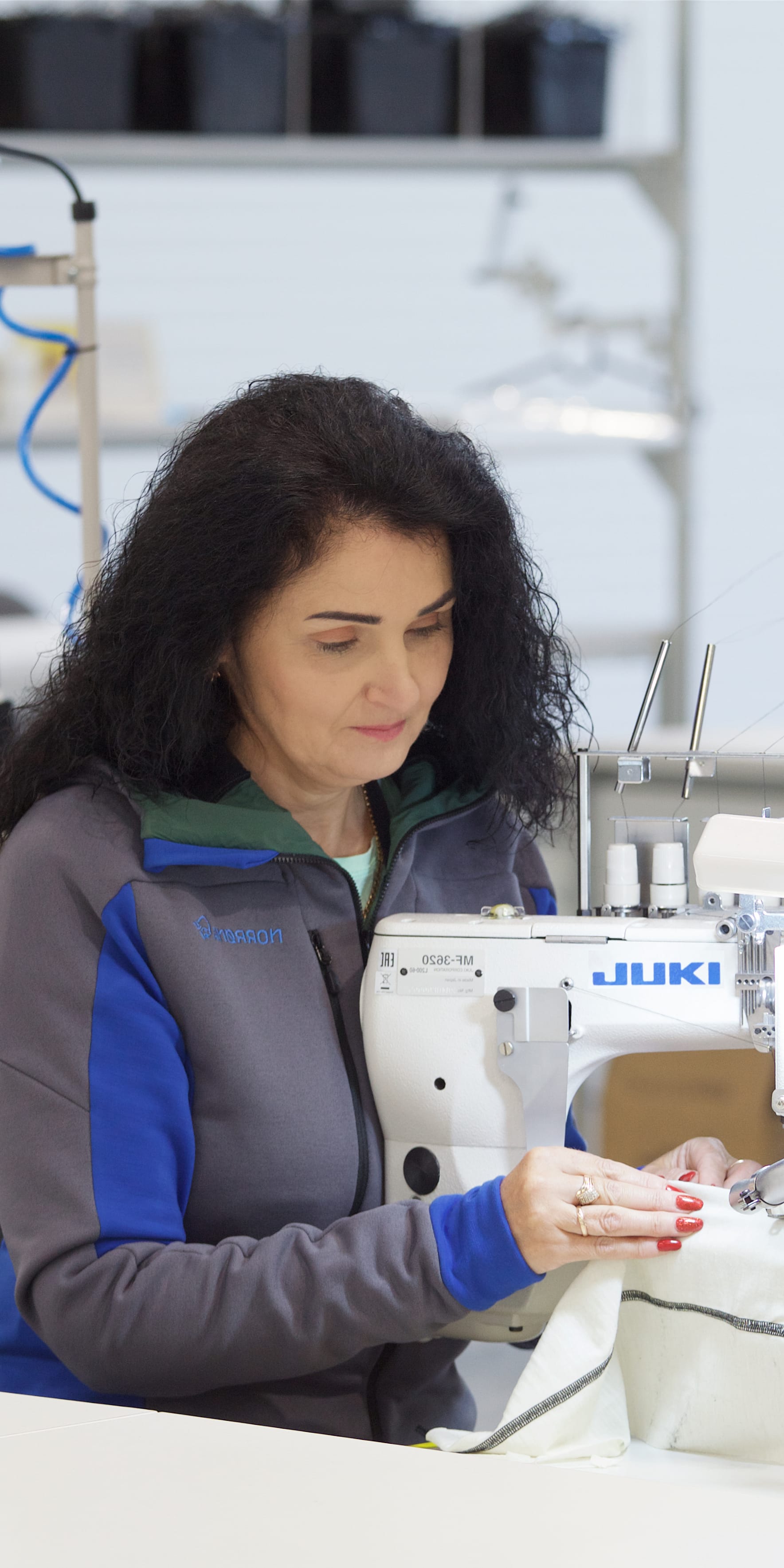 A woman wearing a Norrøna jacket operates a sewing machine. 

