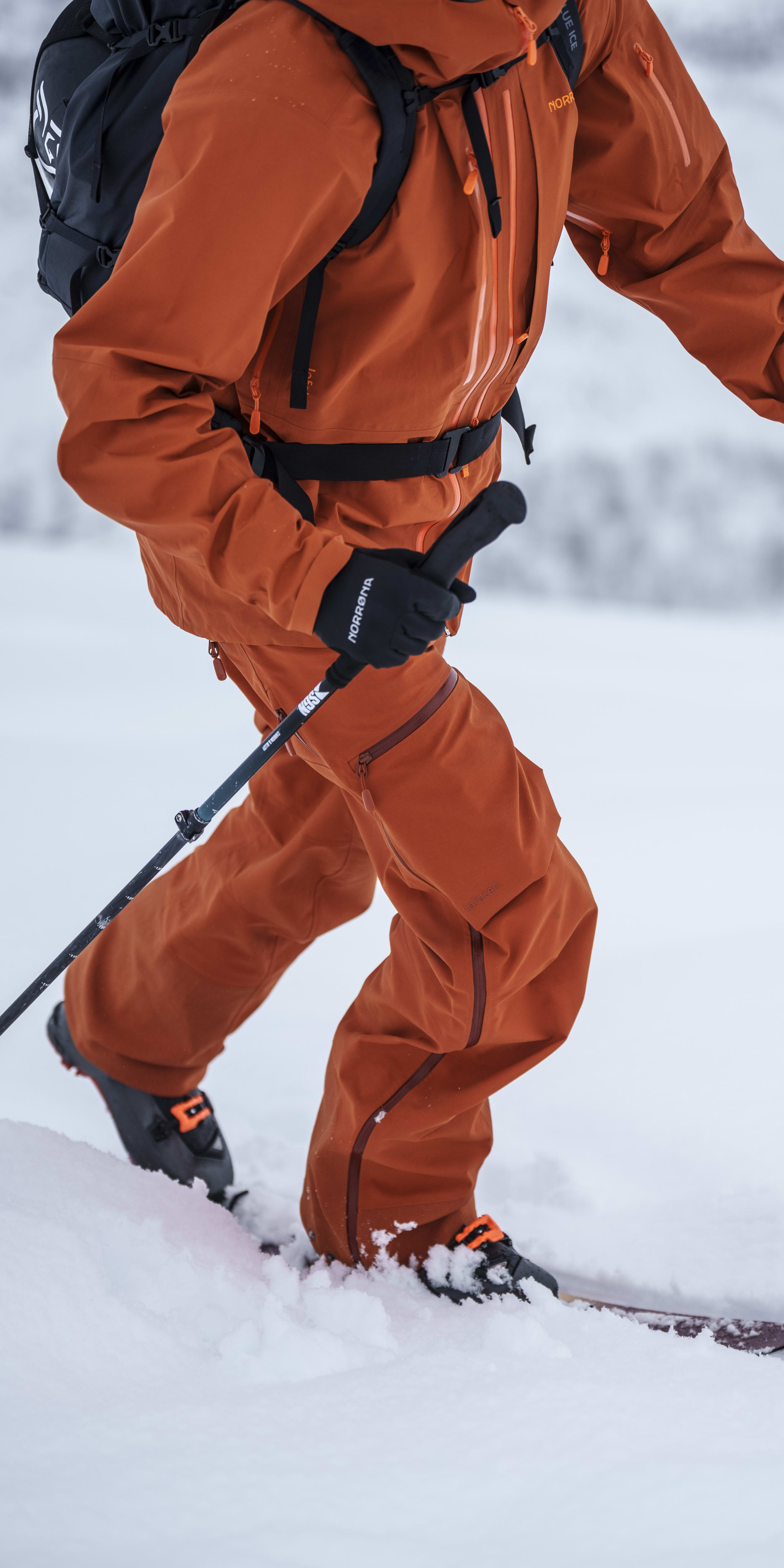 A person wearing a Norrøna jacket and pants skis down a snowy slope. 
