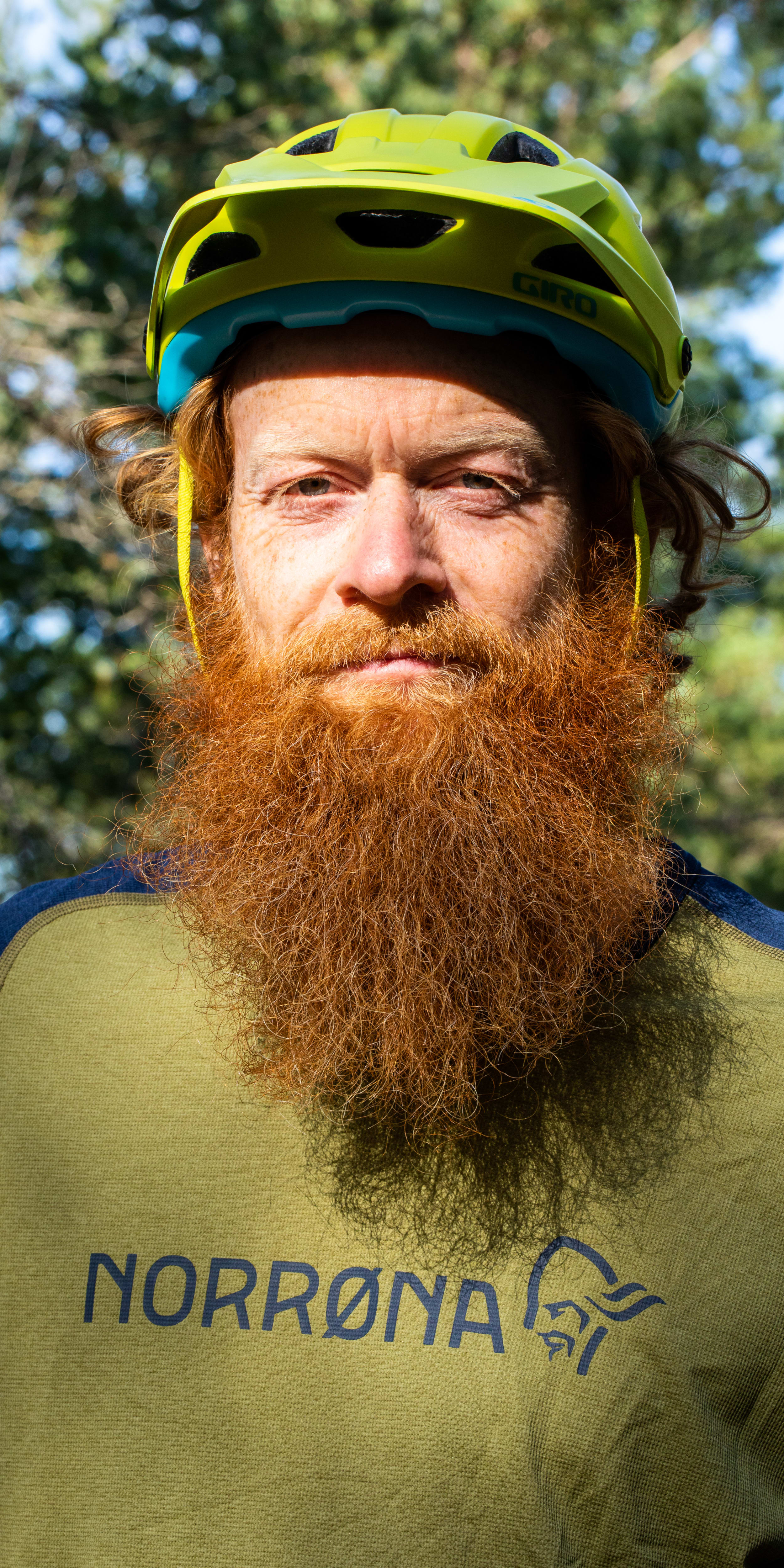 A man with a red beard wearing a Norrøna shirt and a helmet.  
