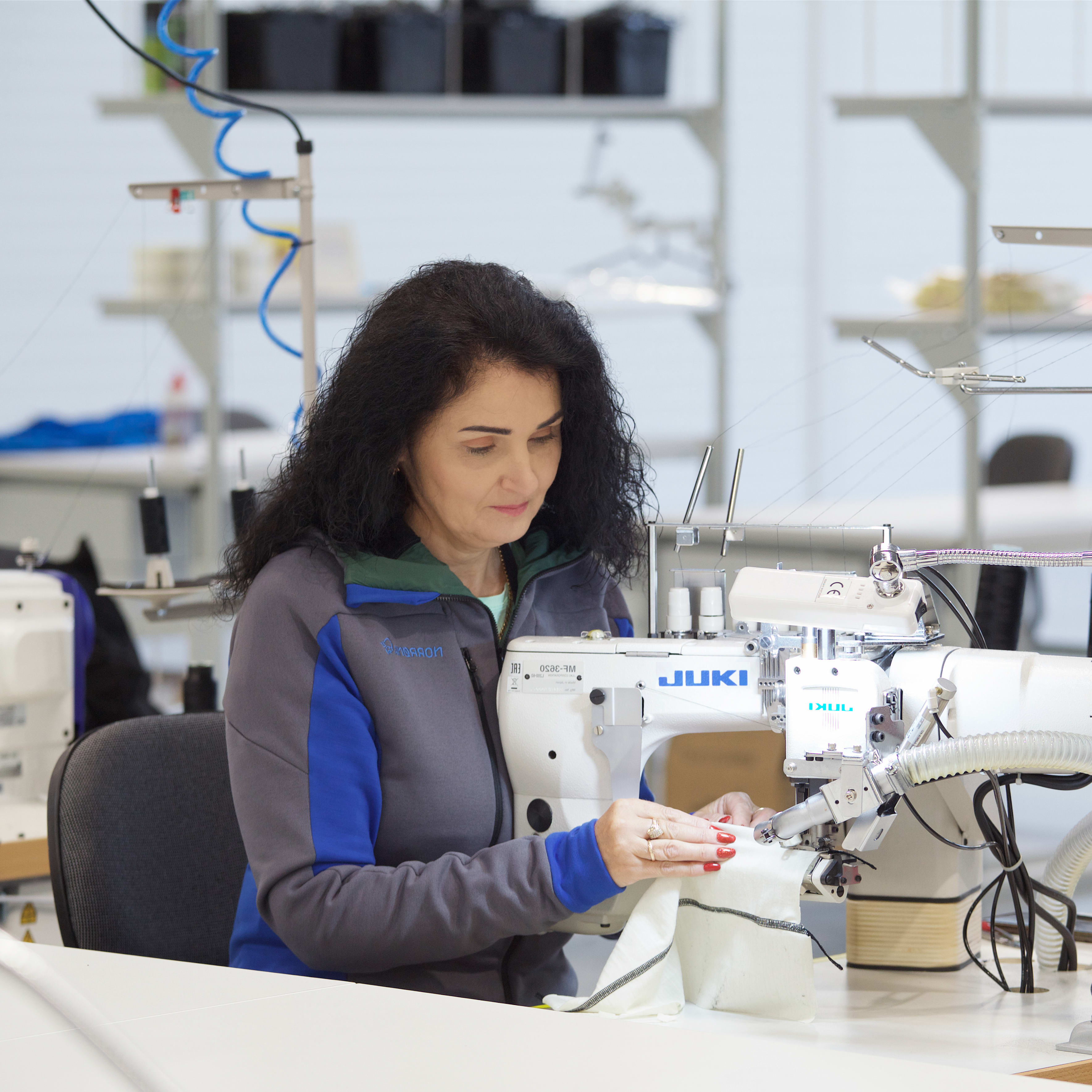A woman wearing a Norrøna jacket operates a sewing machine. 
