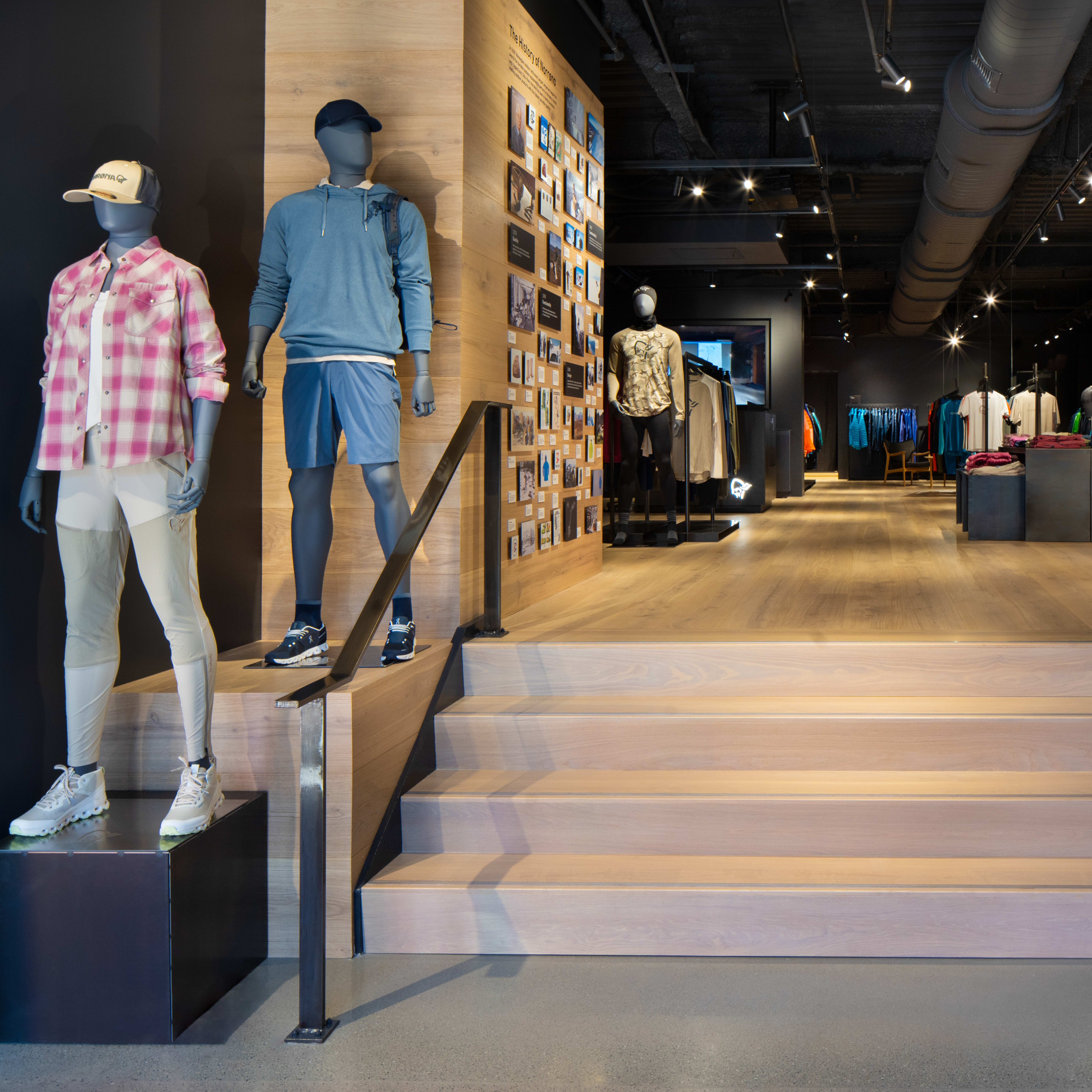 A Norrøna store interior with mannequins wearing clothing, a wooden staircase, and a display of Norrøna apparel. 
