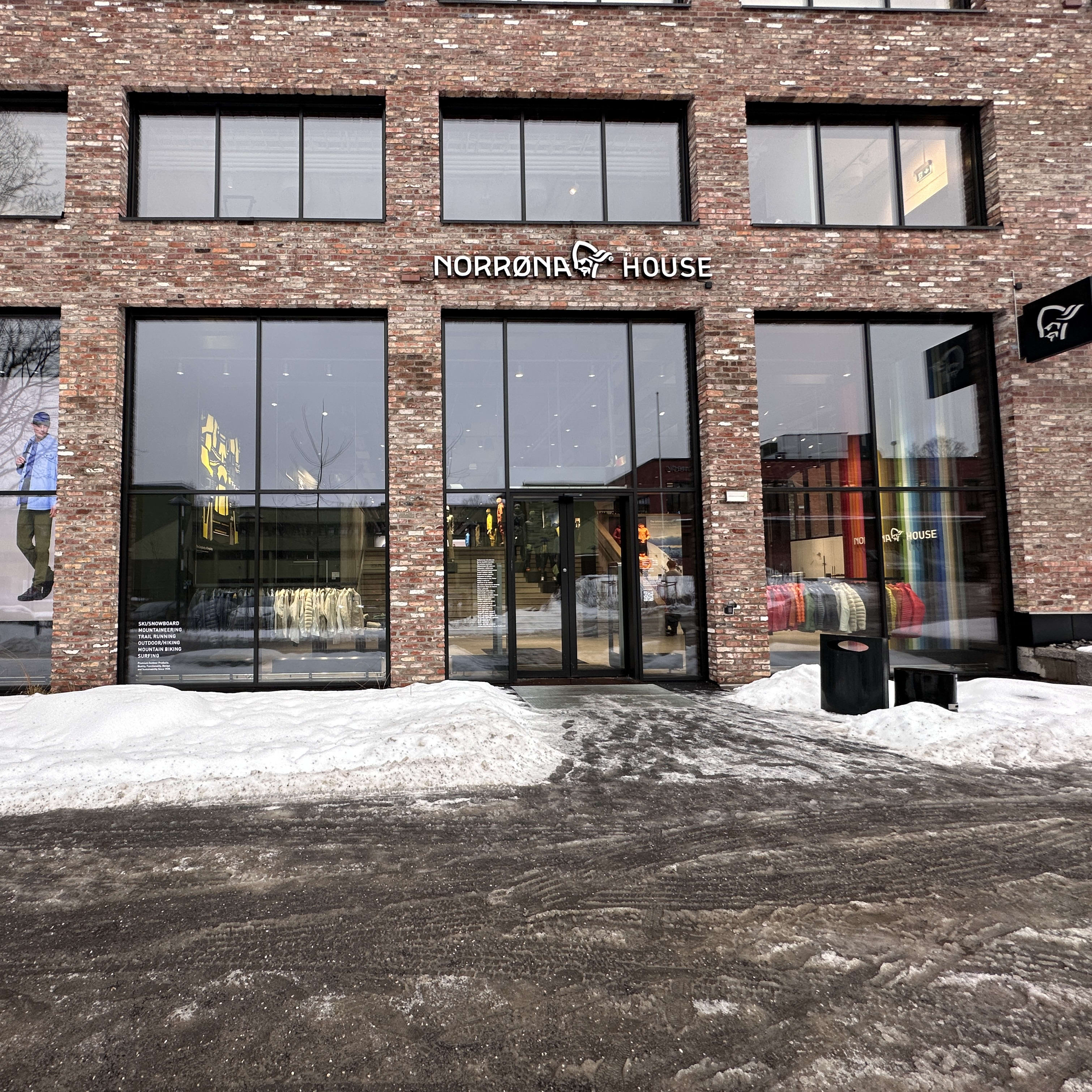 "Exterior of Norrøna House store in winter. Brick building with large windows displaying Norrøna apparel. Signage is visible."